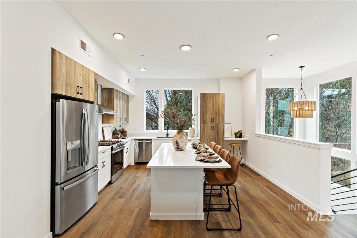 Kitchen with stainless steel appliances, a kitchen bar, light wood-type flooring, decorative light fixtures, and wall chimney range hood