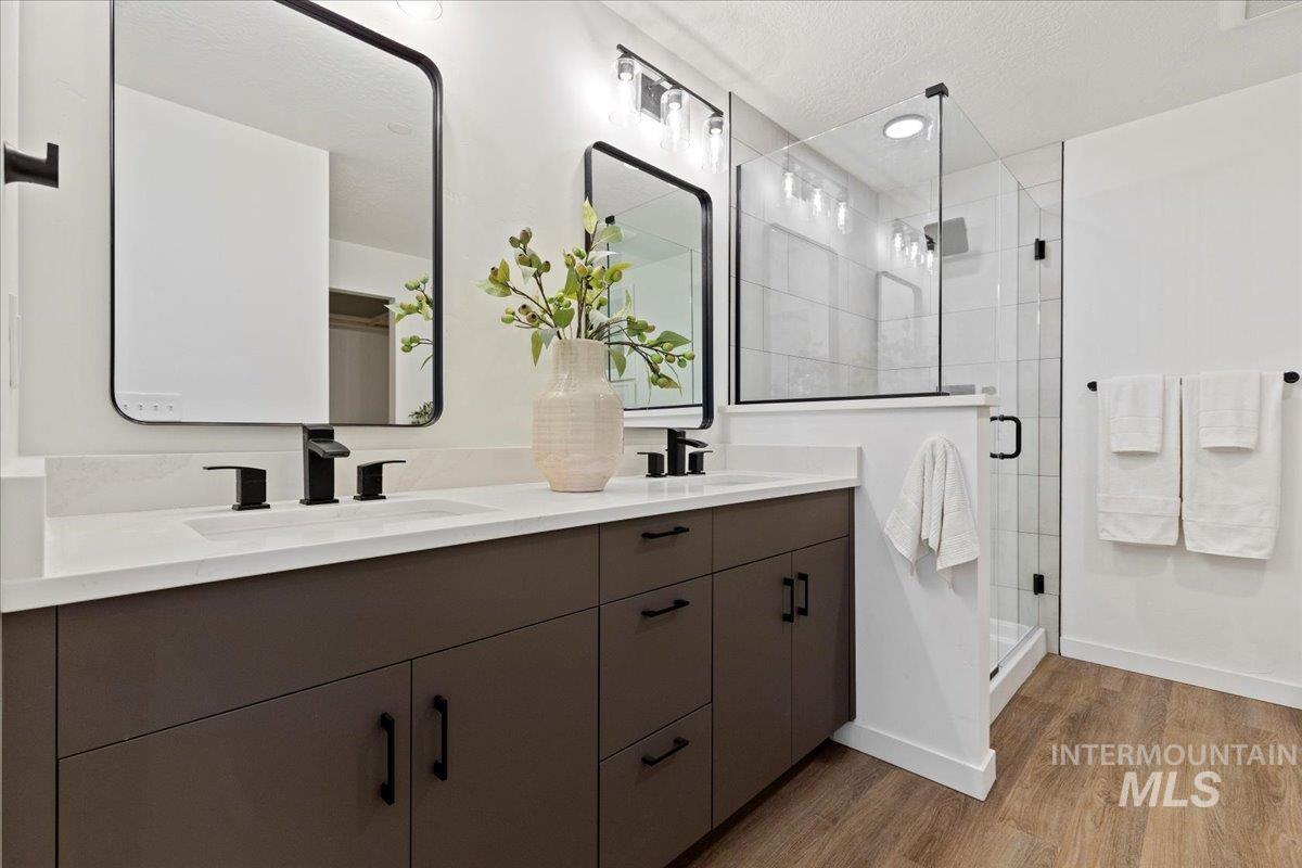 Full bath featuring a shower stall, double vanity, light wood-type flooring, and a textured ceiling