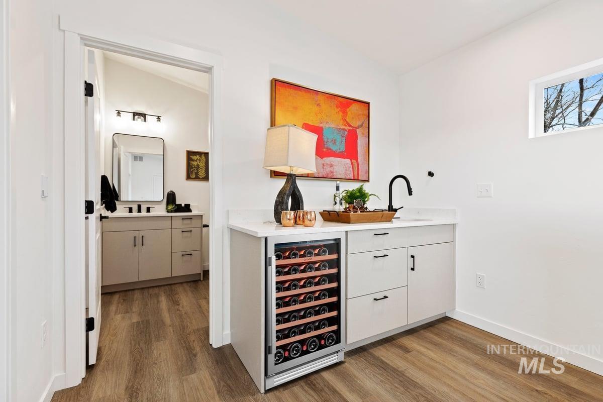 Indoor wet bar featuring white cabinets, beverage cooler, dark wood-type flooring, and light stone counters