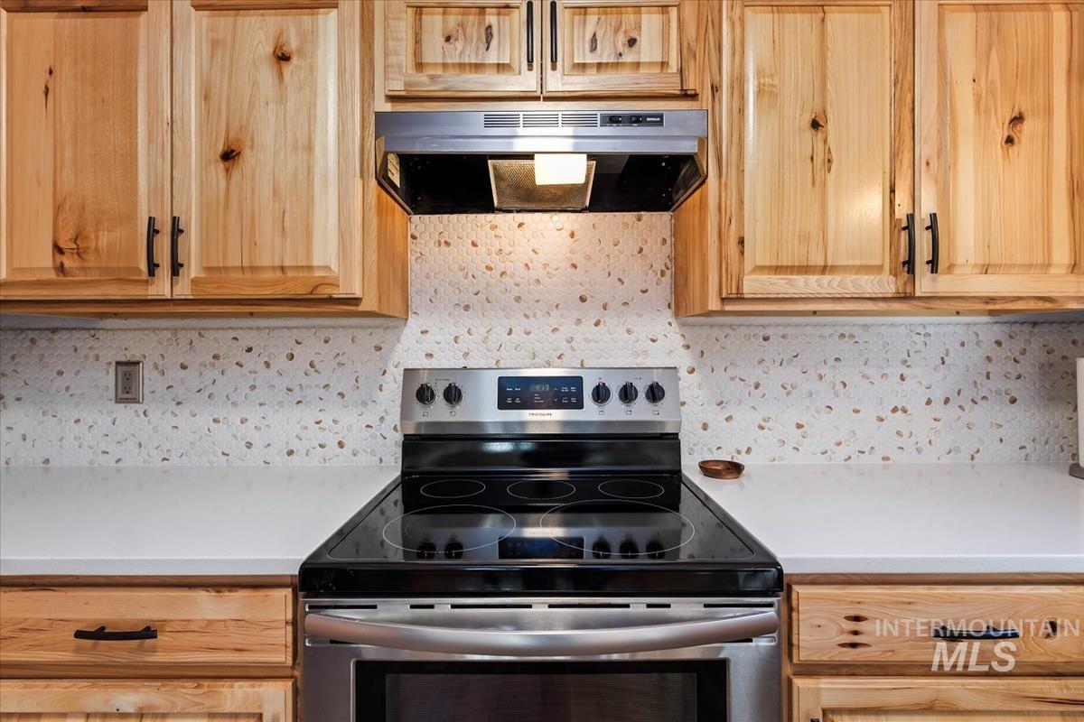 Kitchen with stainless steel electric stove, light countertops, range hood, and backsplash