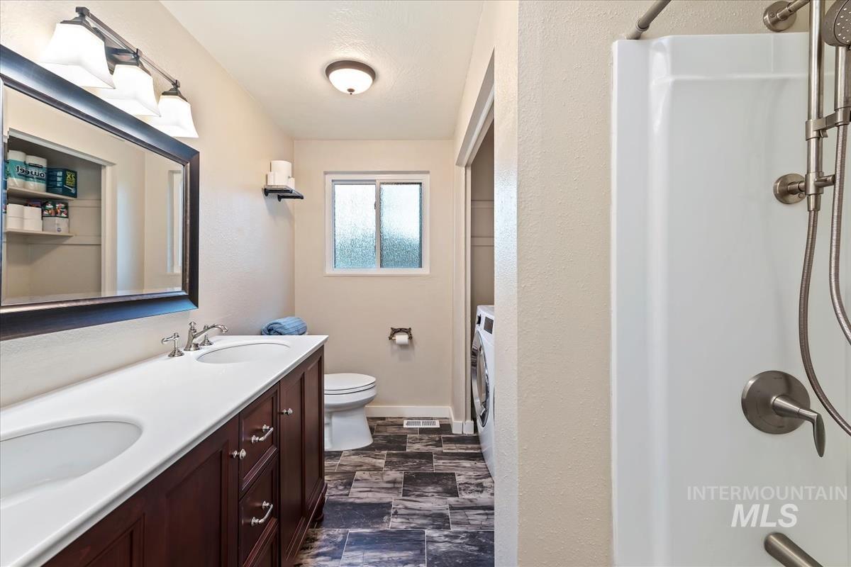 Bathroom featuring double vanity, a shower with shower curtain, a textured wall, washer / clothes dryer, and dark stone finish floors