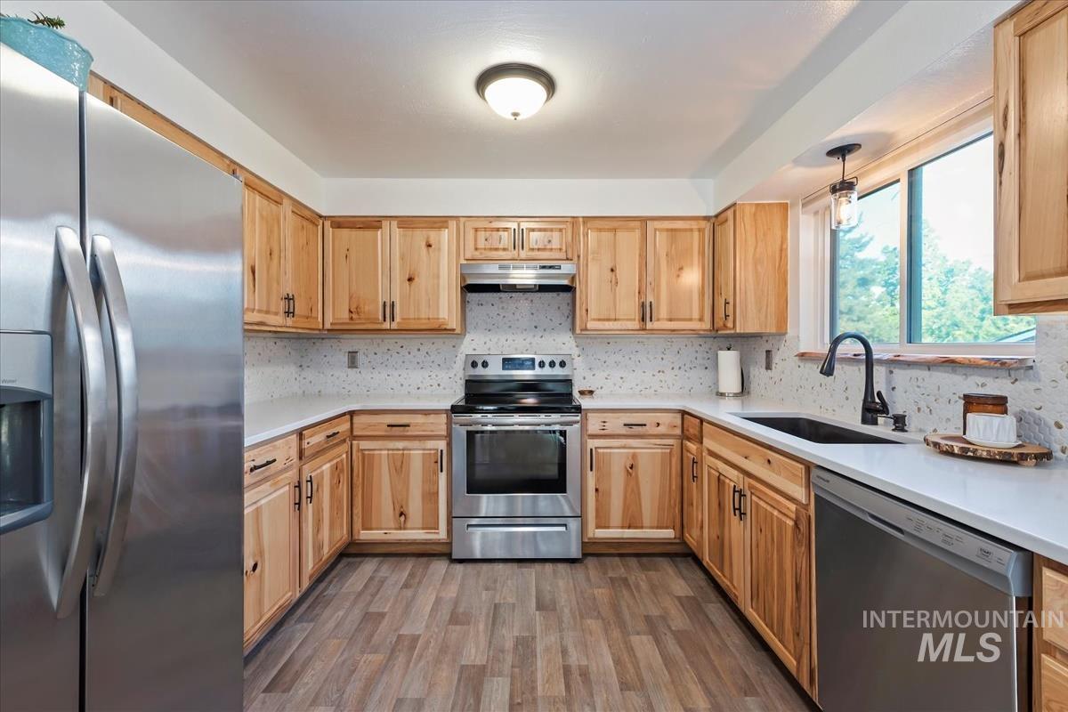 Kitchen featuring appliances with stainless steel finishes, decorative backsplash, dark wood-style flooring, and under cabinet range hood