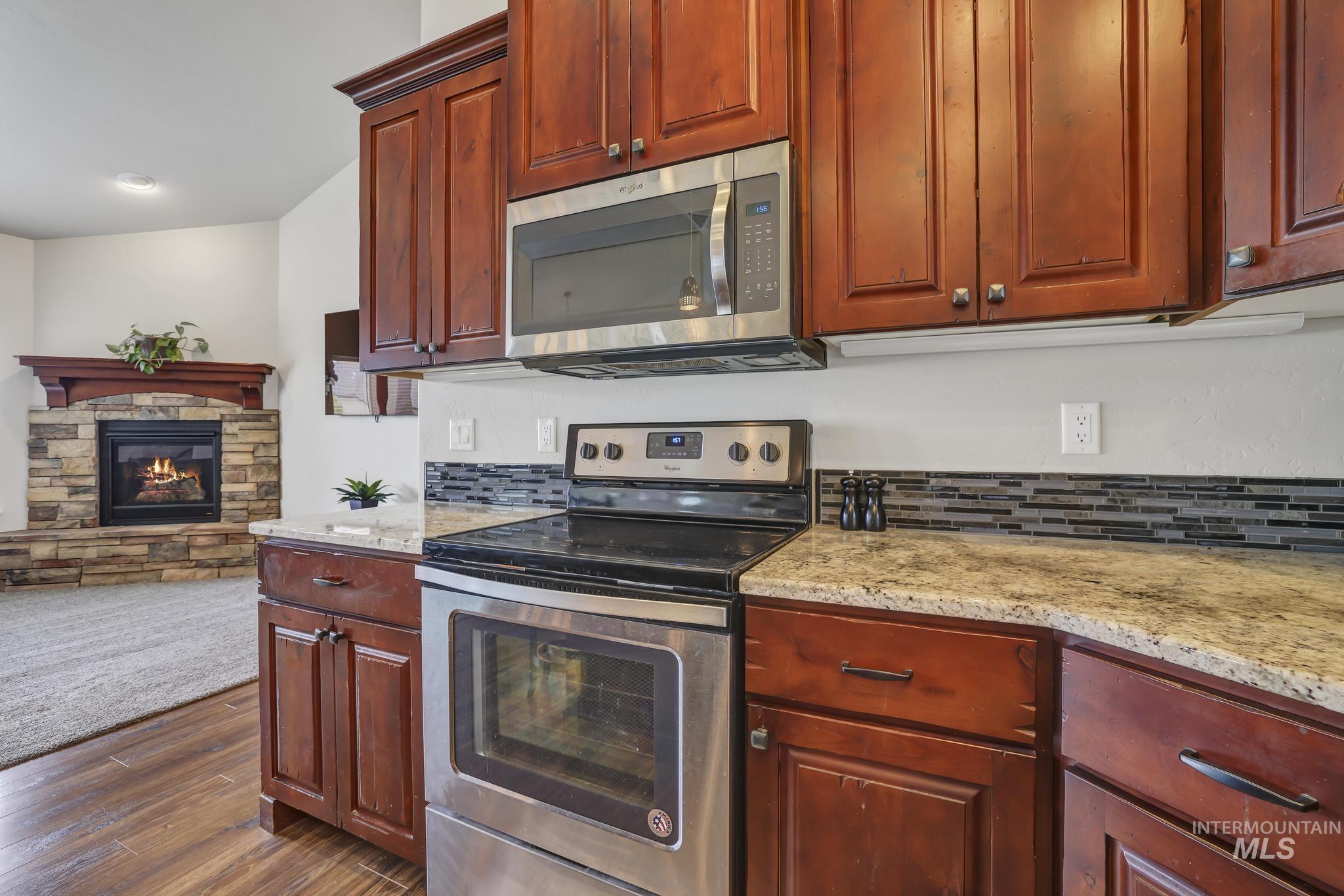 Kitchen with appliances with stainless steel finishes, light stone countertops, a fireplace, dark wood finished floors, and backsplash