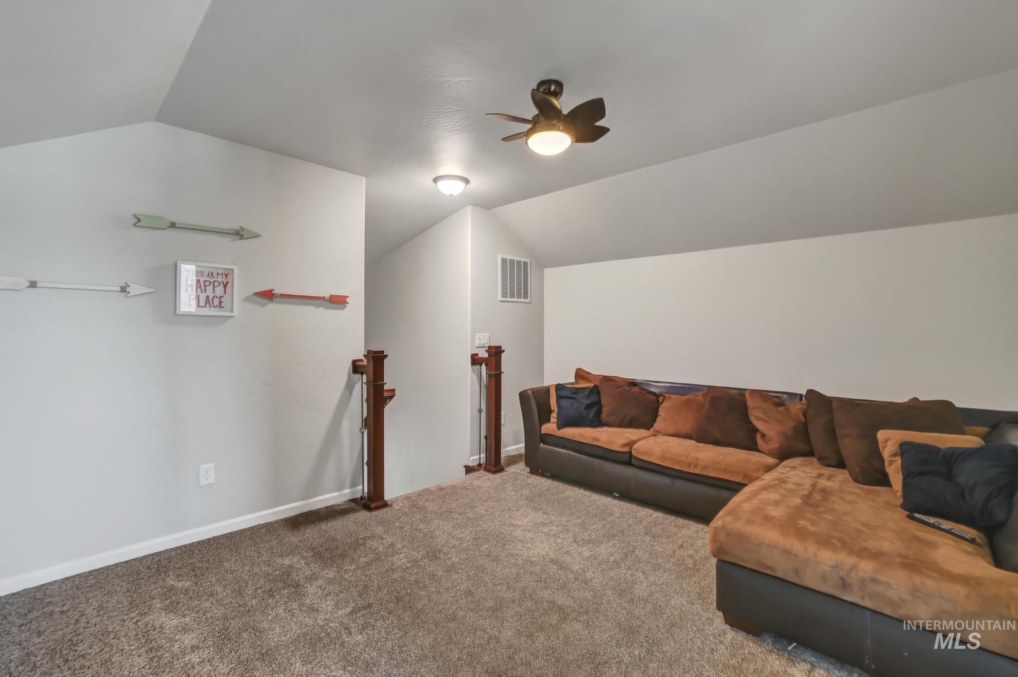 Living area featuring vaulted ceiling, carpet flooring, and a ceiling fan