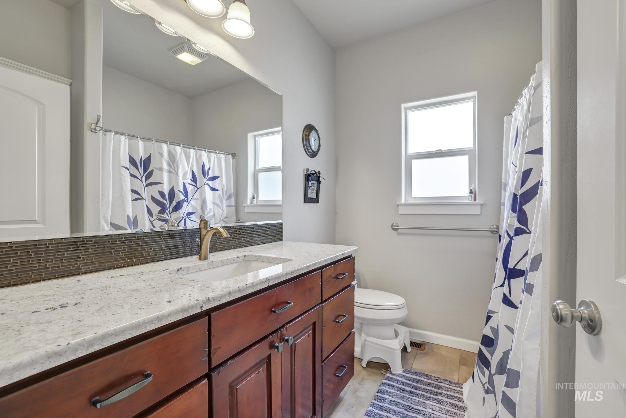 Bathroom featuring vanity, decorative backsplash, light tile patterned floors, and curtained shower