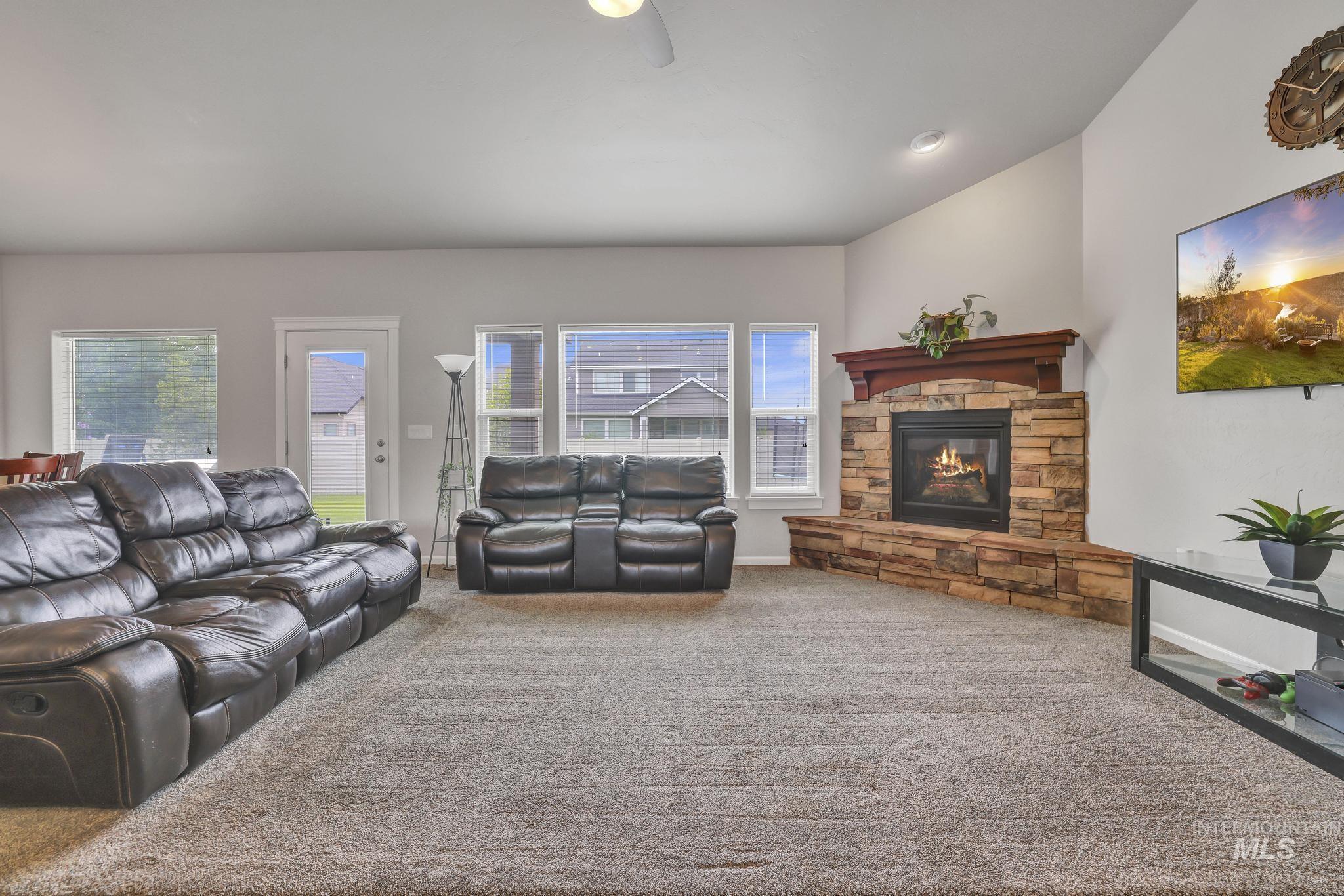 Living area with carpet flooring, a stone fireplace, and ceiling fan