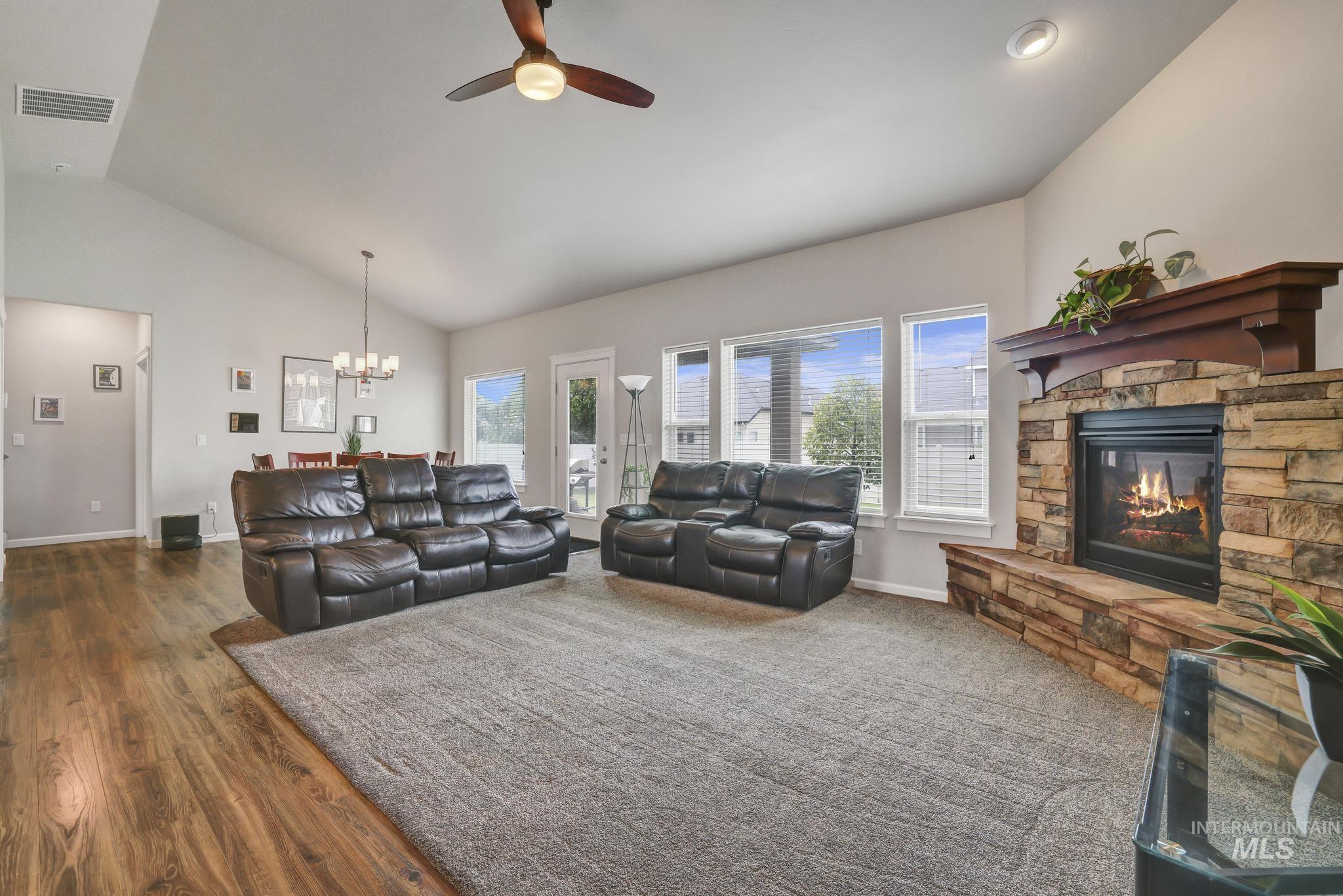 Living area with plenty of natural light, a ceiling fan, high vaulted ceiling, dark wood-style floors, and a chandelier