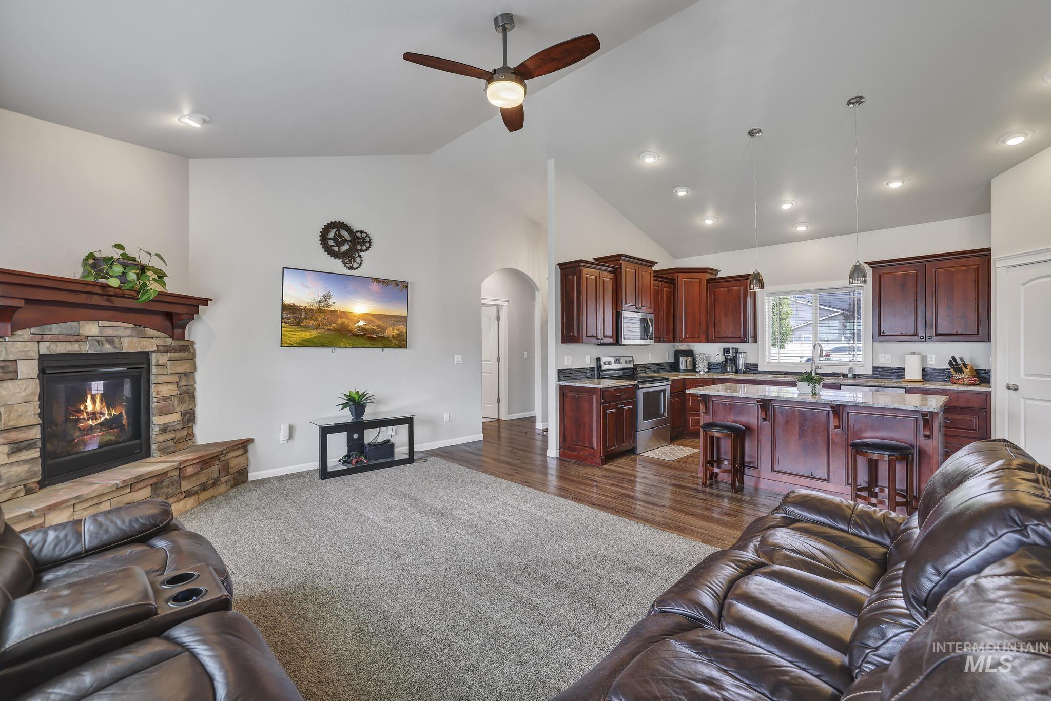 Living area with arched walkways, dark wood-type flooring, ceiling fan, a fireplace, and high vaulted ceiling