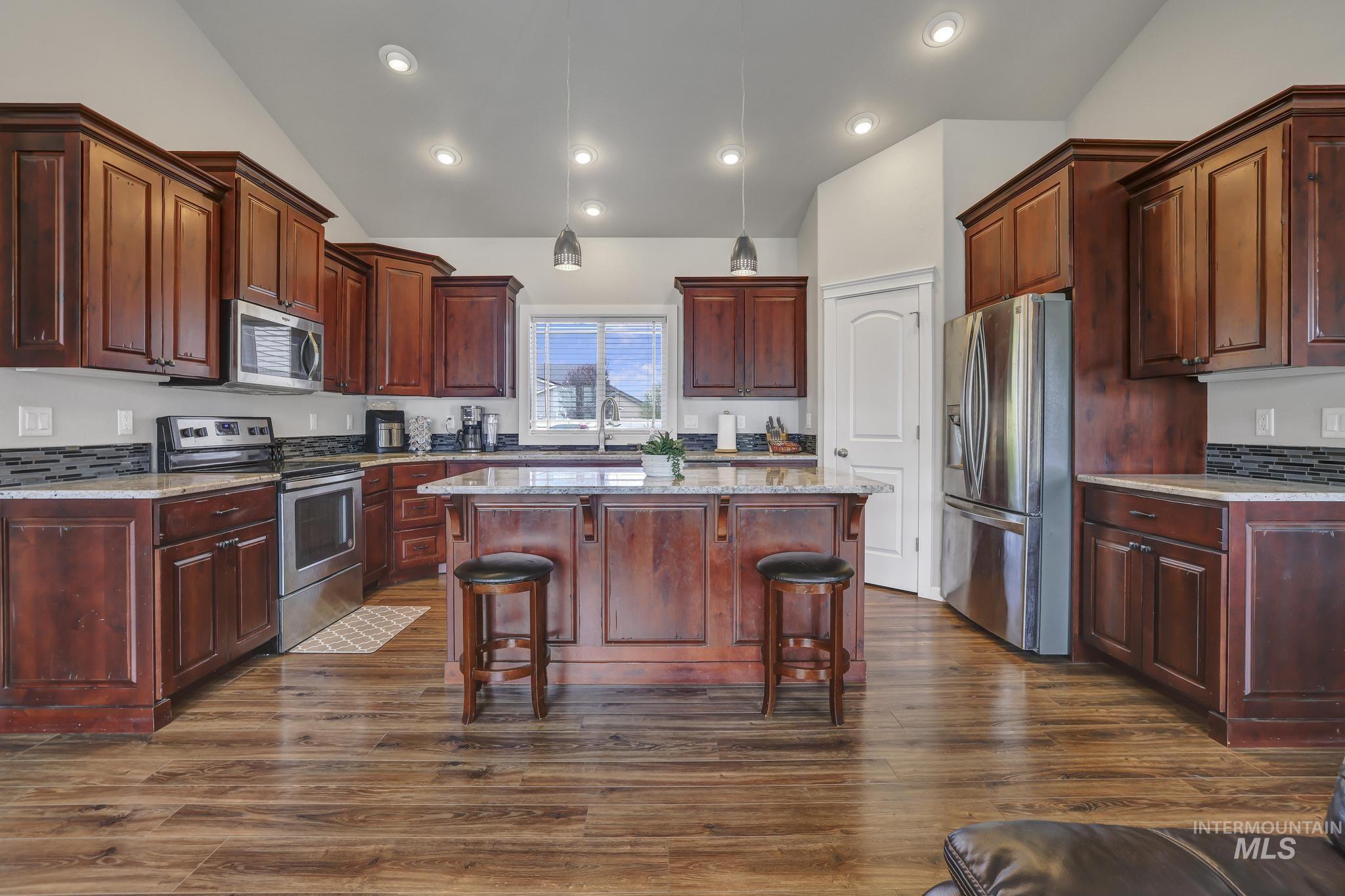 Kitchen with stainless steel appliances, pendant lighting, light stone counters, dark wood finished floors, and vaulted ceiling