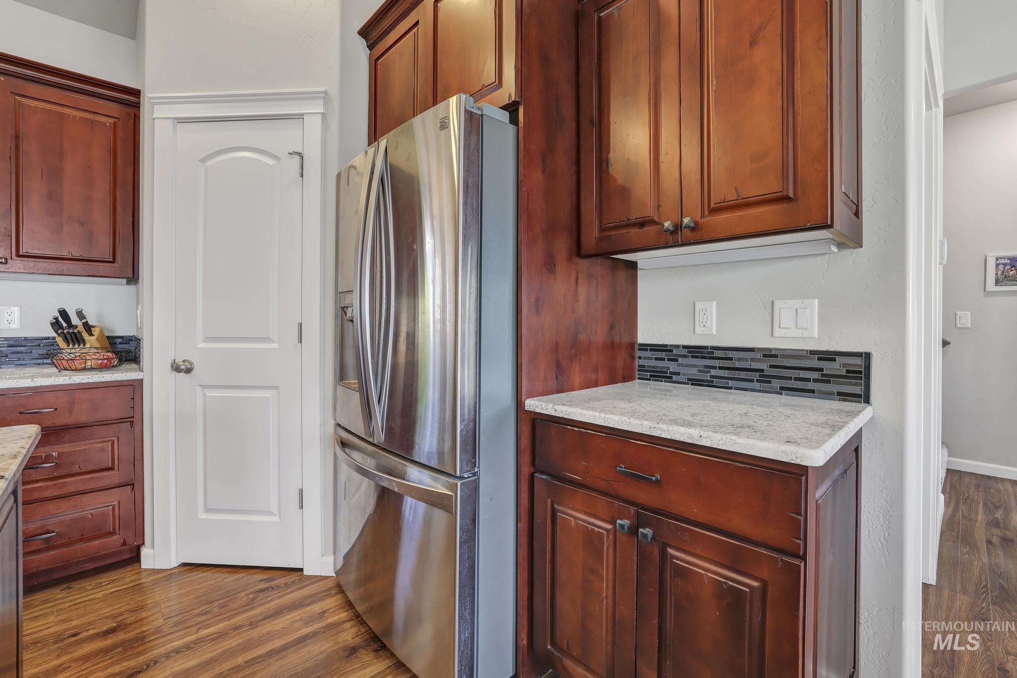 Kitchen with stainless steel fridge with ice dispenser, dark wood-type flooring, light stone countertops, and decorative backsplash