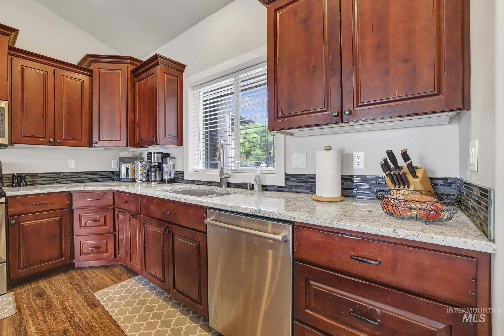 Kitchen featuring light stone countertops, dishwasher, dark wood-style floors, vaulted ceiling, and dark brown cabinets