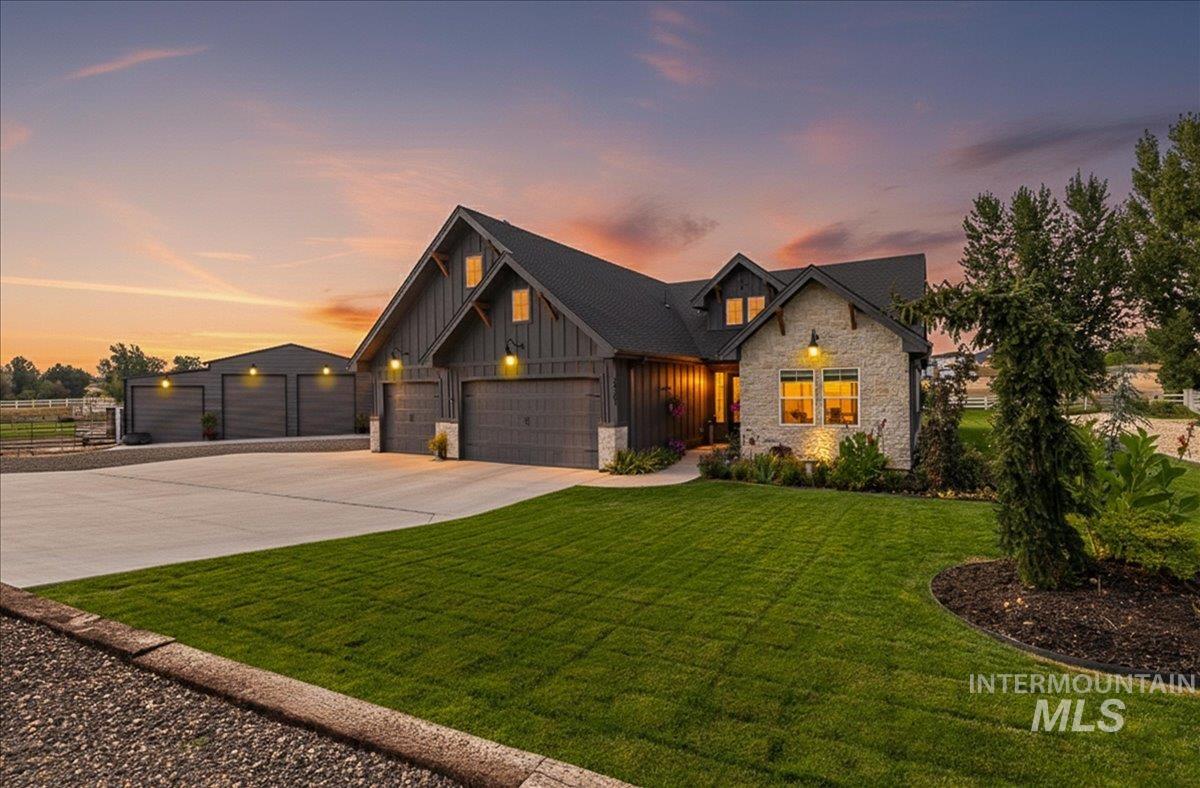 View of front of property featuring stone siding, board and batten siding, driveway, a front yard, and a garage