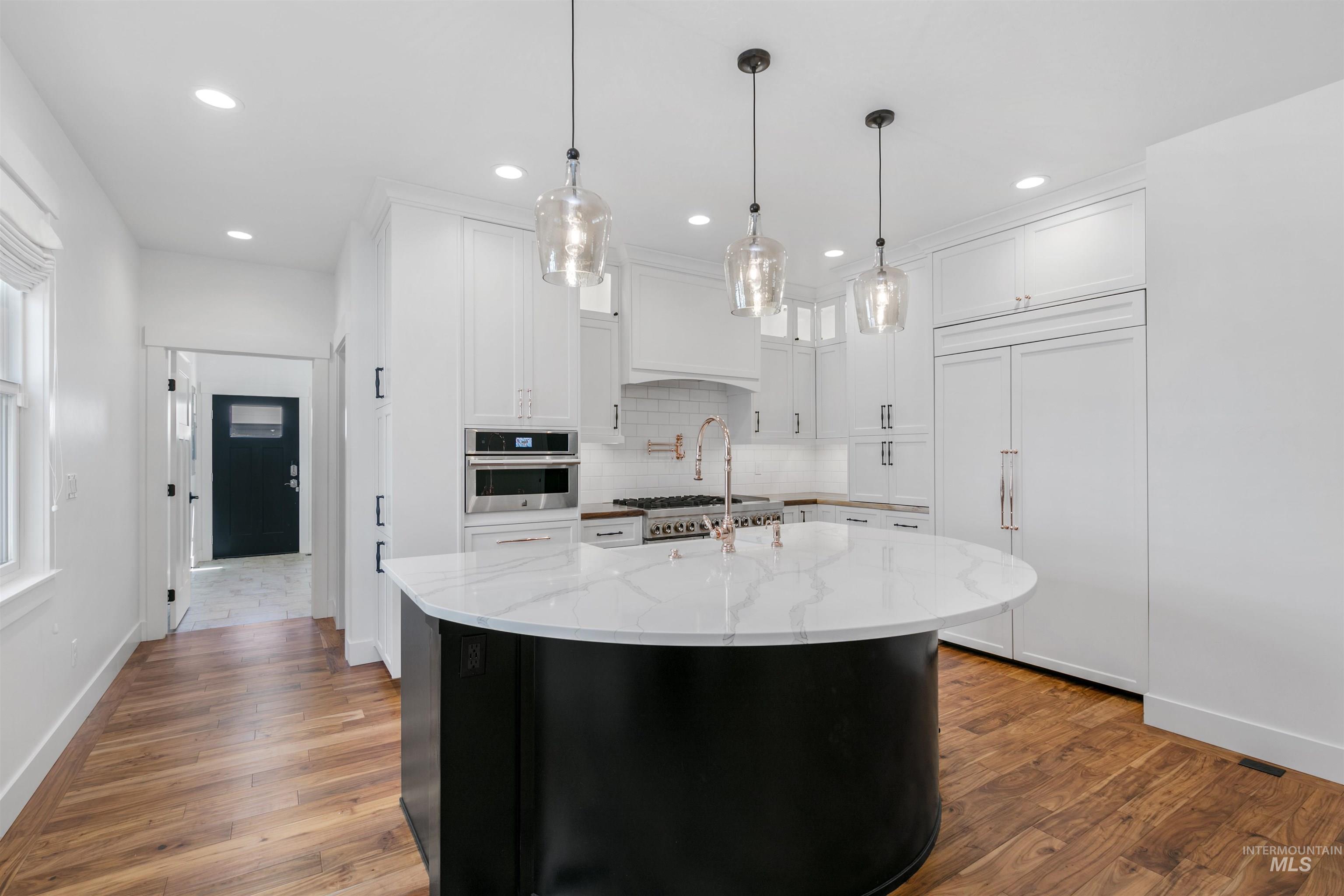 Kitchen with white cabinets, decorative backsplash, dark cabinets, a center island with sink, and dark wood finished floors