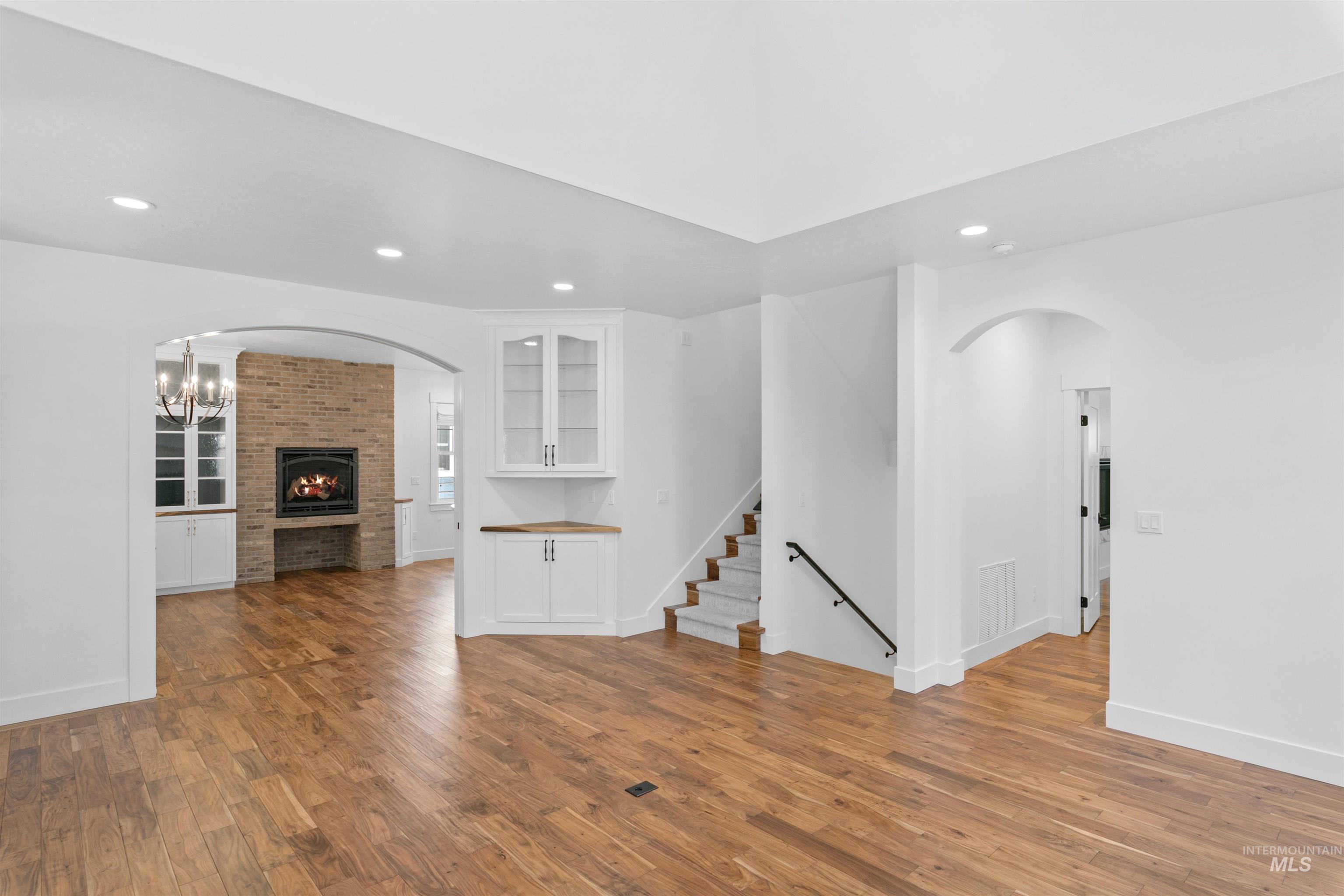 Unfurnished living room with arched walkways, recessed lighting, wood finished floors, a chandelier, and stairs