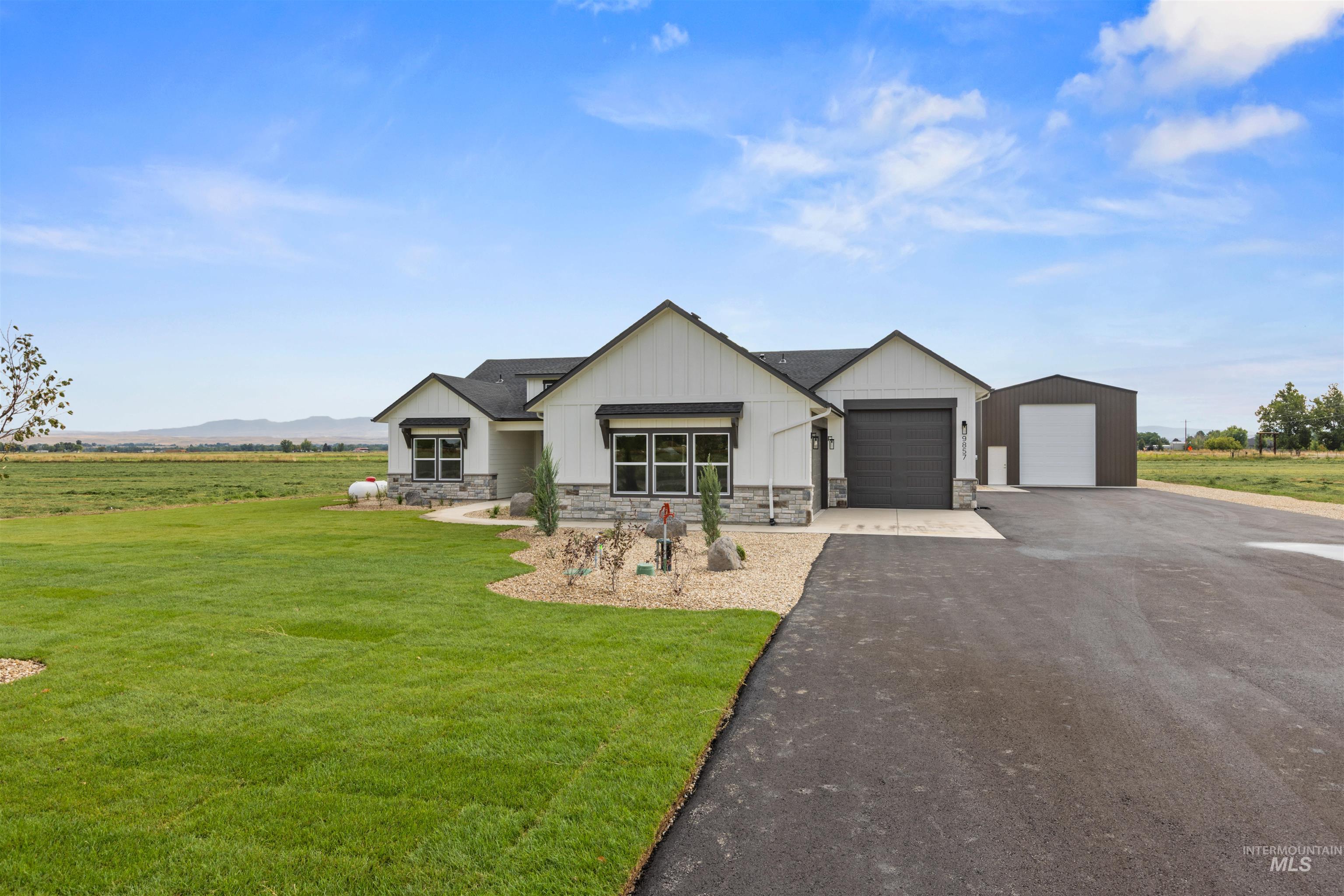 Modern inspired farmhouse with board and batten siding, stone siding, driveway, a rural view, and a front lawn