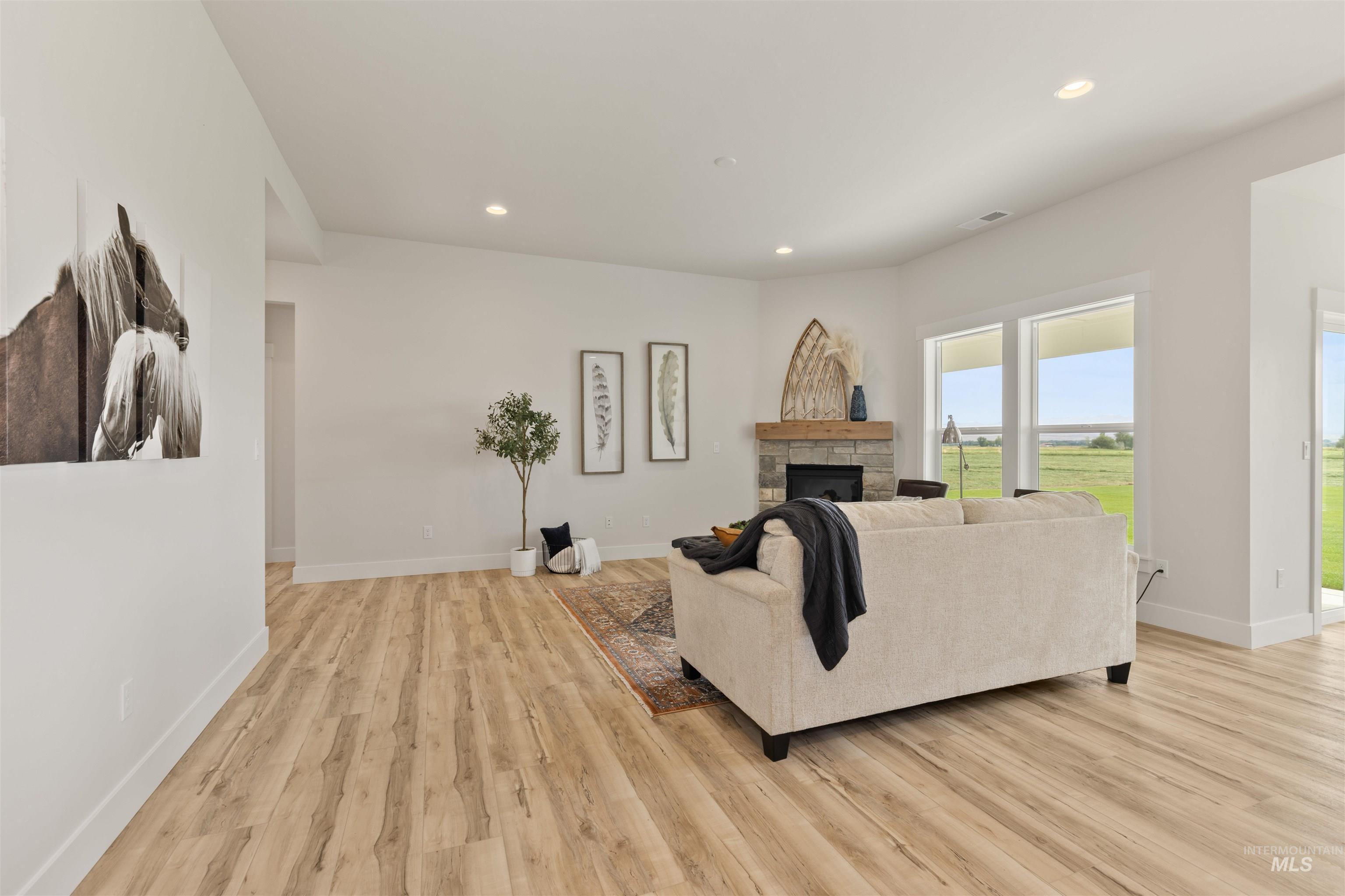 Living area with recessed lighting, a stone fireplace, and light wood-style flooring