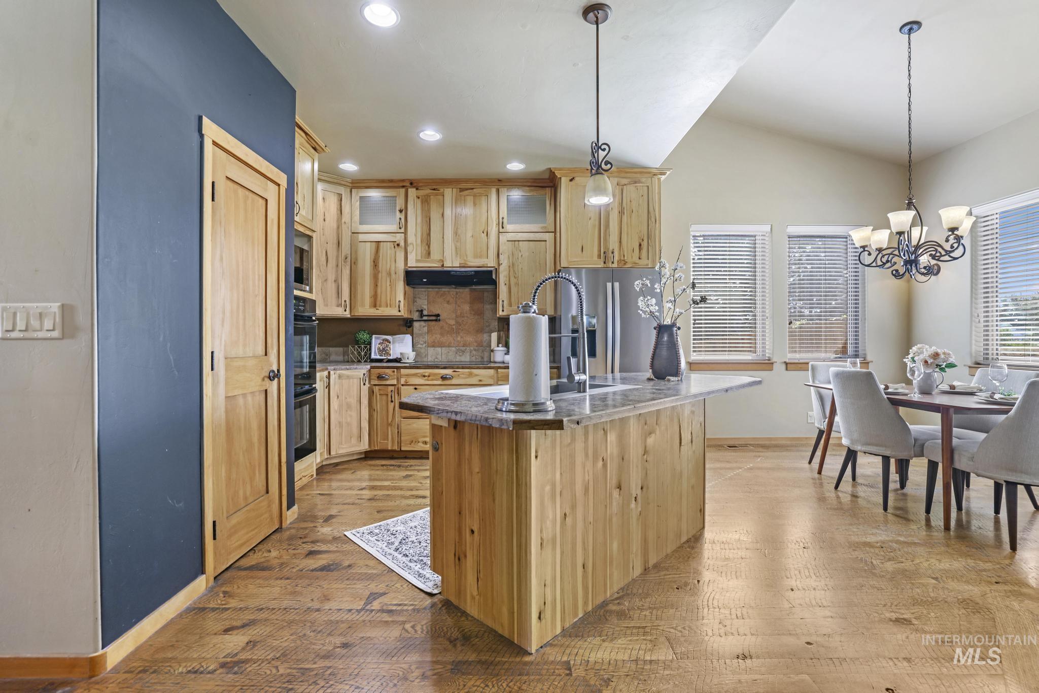 Kitchen featuring light brown cabinets, decorative light fixtures, decorative backsplash, light wood-style flooring, and vaulted ceiling