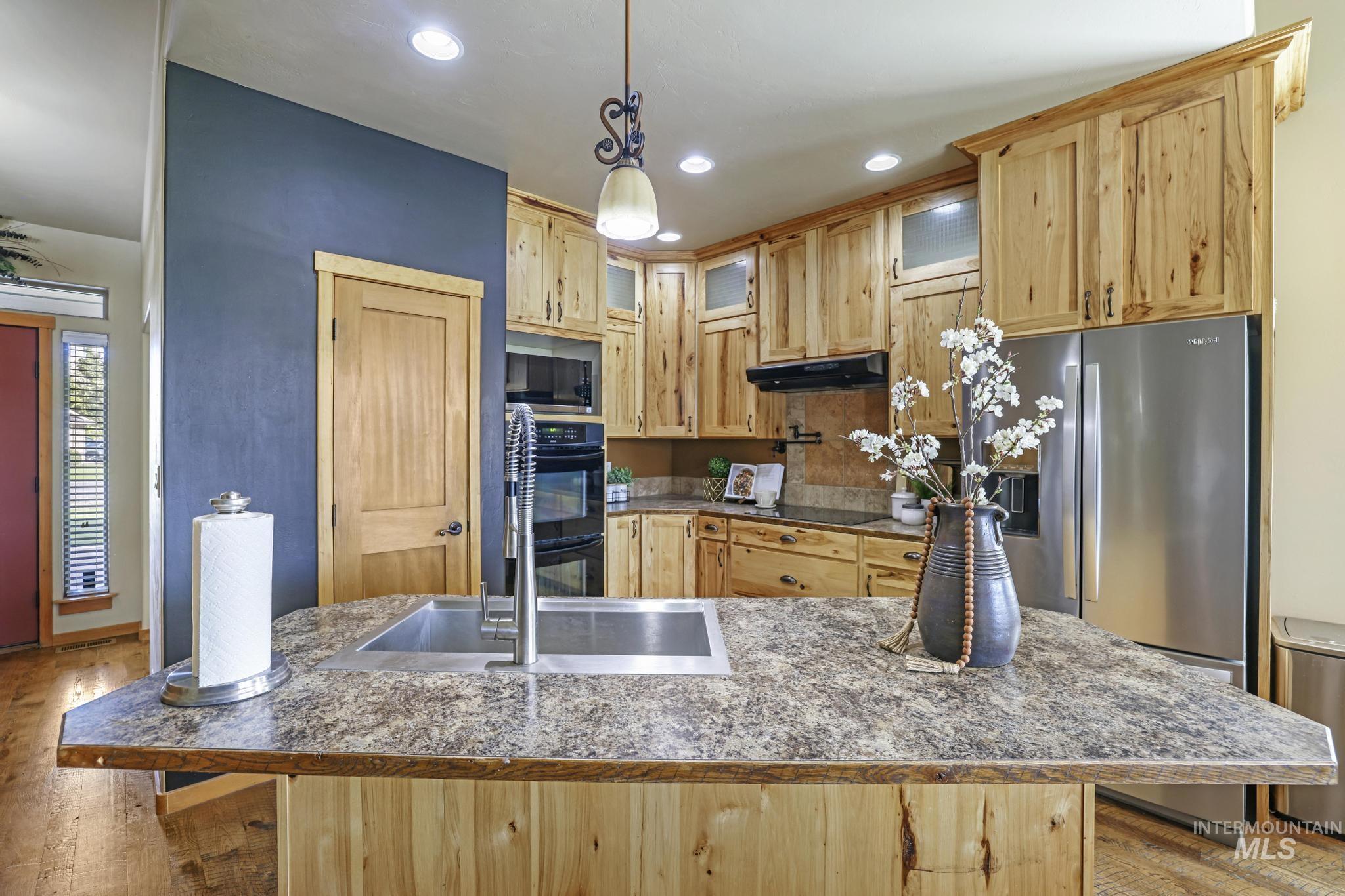 Kitchen featuring light brown cabinetry, stainless steel refrigerator with ice dispenser, decorative light fixtures, light wood-style flooring, and recessed lighting