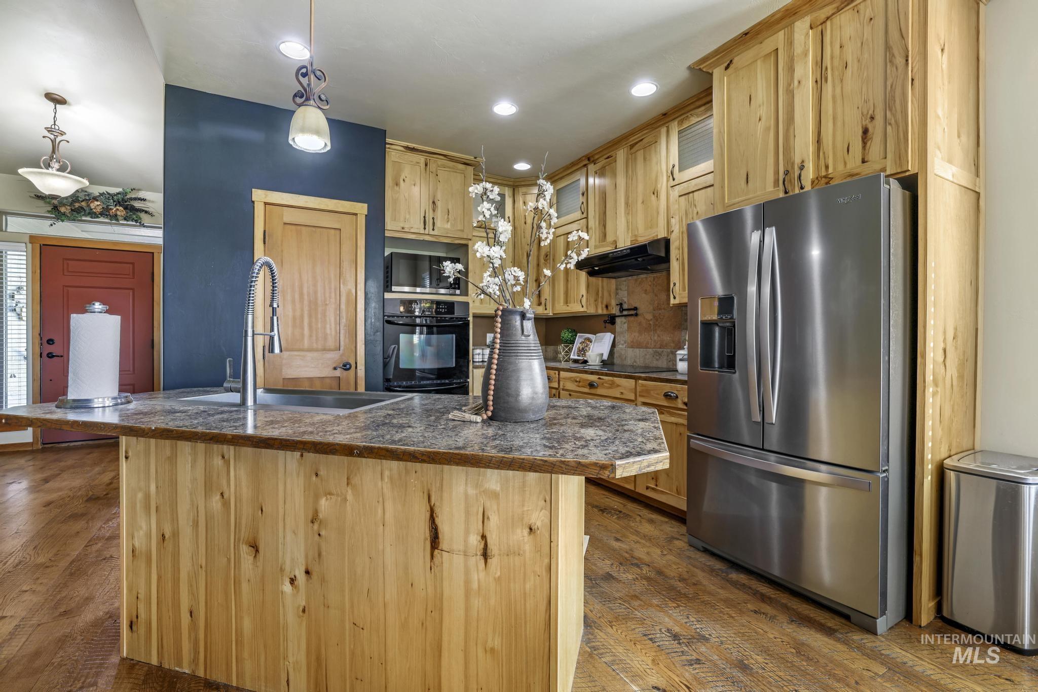 Kitchen featuring dark countertops, black appliances, hanging light fixtures, dark wood-style floors, and light brown cabinets