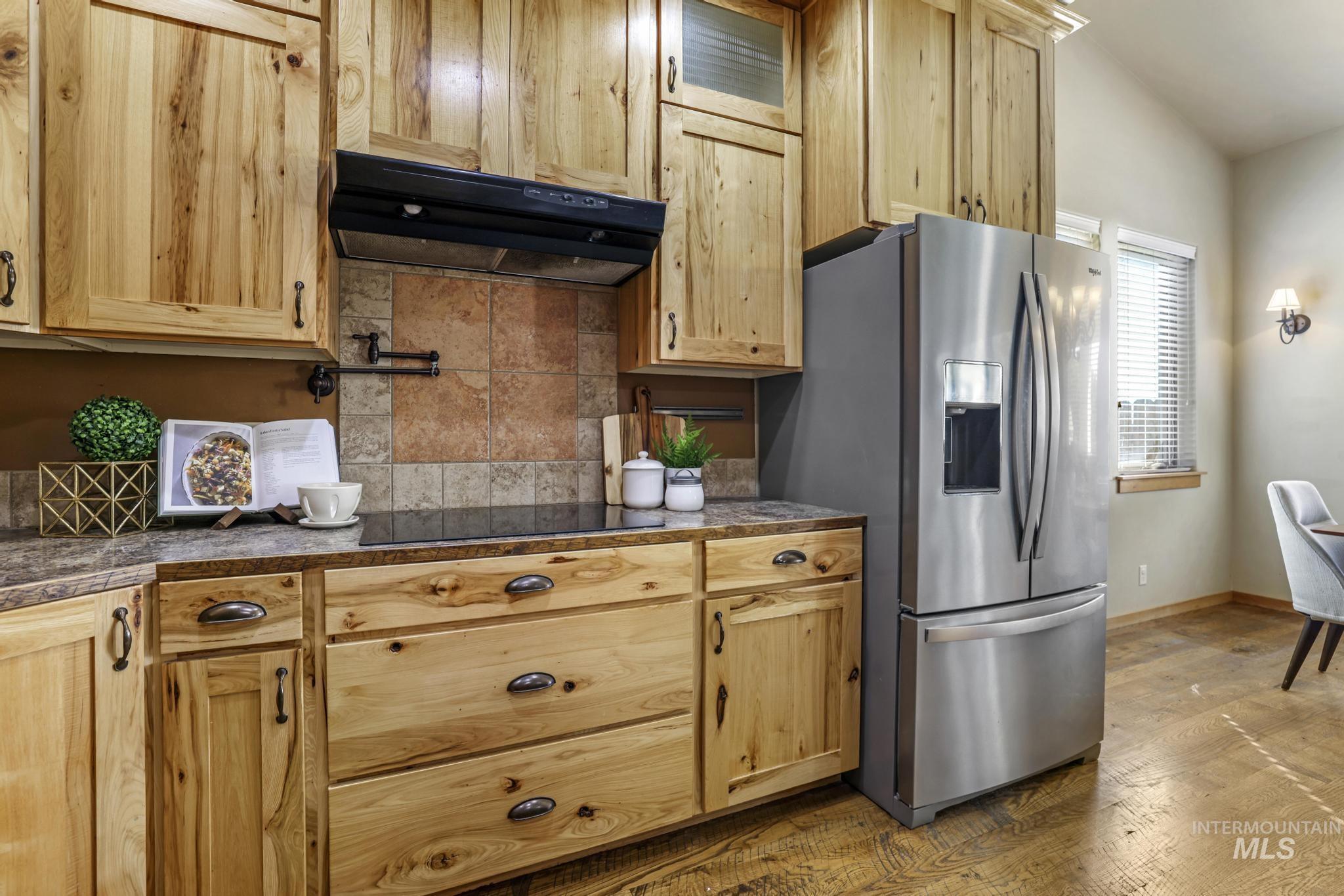 Kitchen with under cabinet range hood, decorative backsplash, dark wood-type flooring, stainless steel refrigerator with ice dispenser, and tile counters