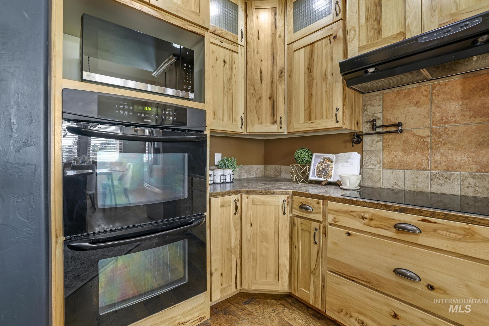 Kitchen featuring black appliances, under cabinet range hood, and light brown cabinets