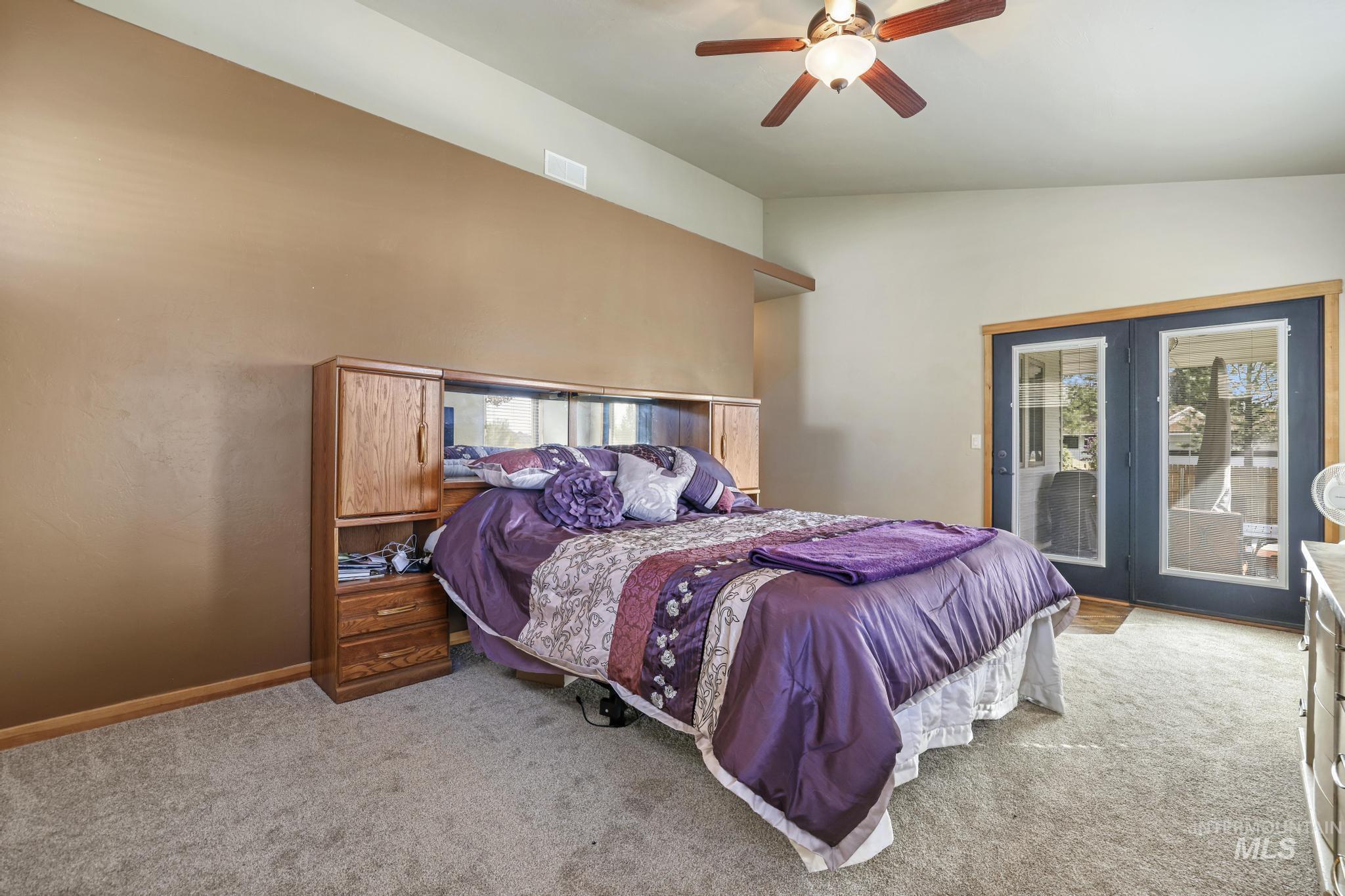 Carpeted bedroom with access to exterior, vaulted ceiling, and a ceiling fan