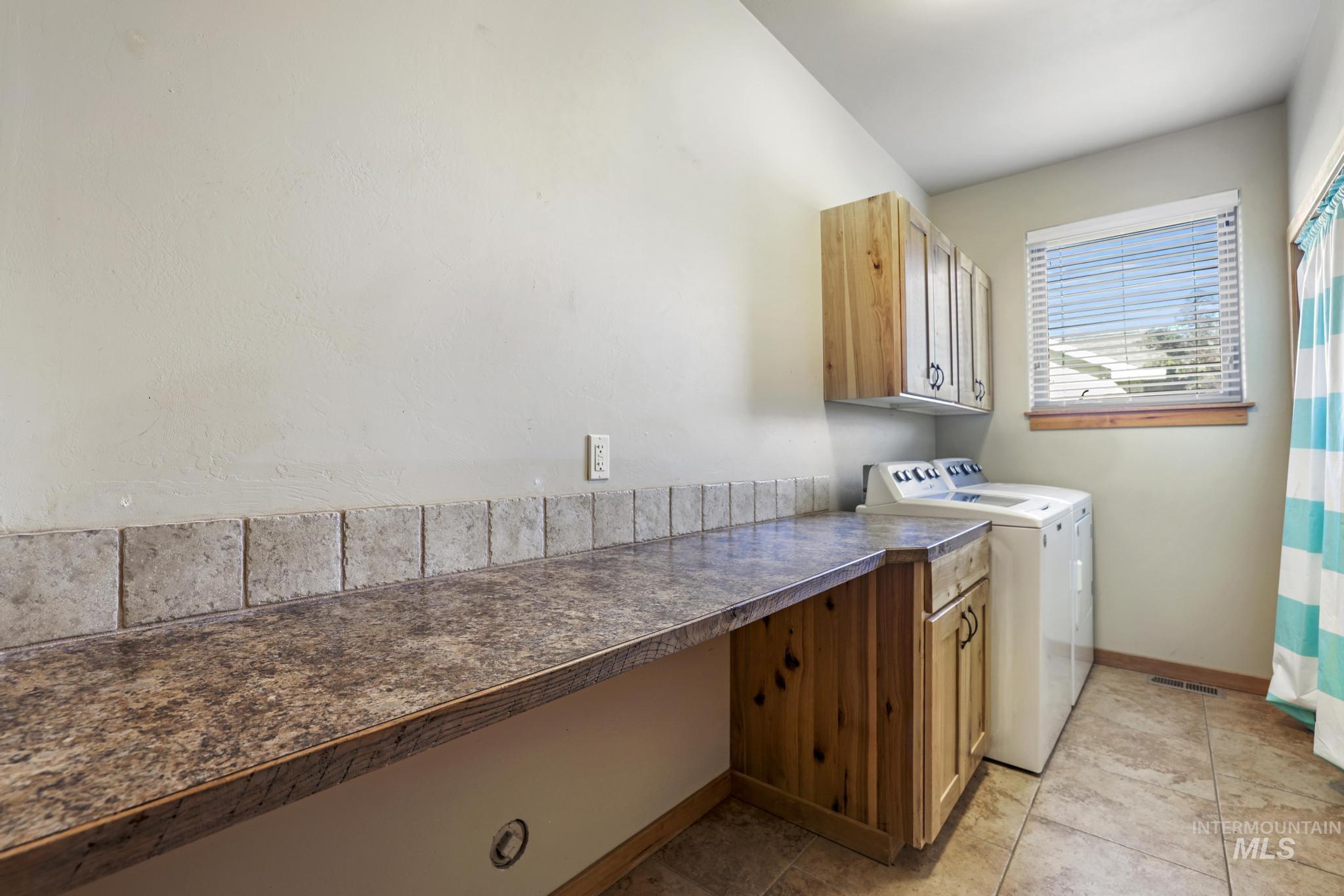 Laundry room with independent washer and dryer, light tile patterned floors, and cabinet space