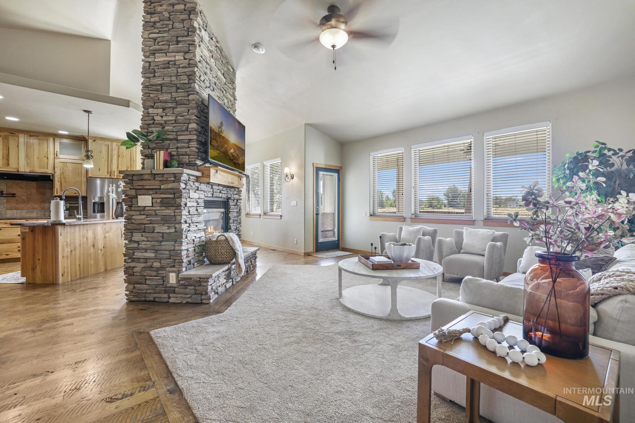 Living room featuring a ceiling fan, dark wood-style flooring, a stone fireplace, and vaulted ceiling