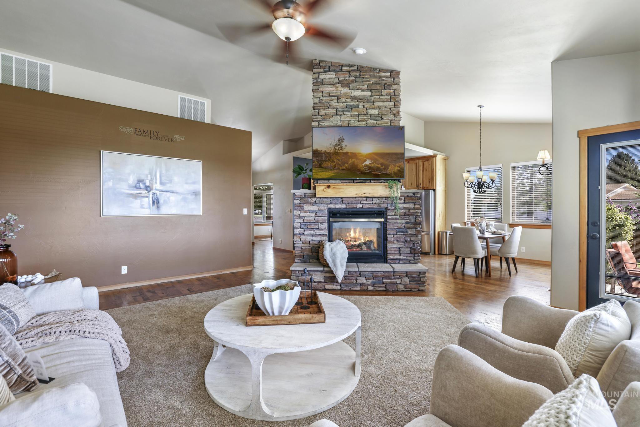 Living room with wood finished floors, a fireplace, lofted ceiling, ceiling fan, and a chandelier