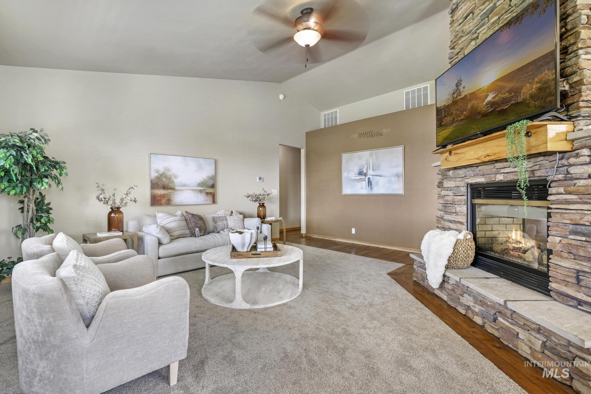 Living area with vaulted ceiling, wood finished floors, ceiling fan, and a stone fireplace