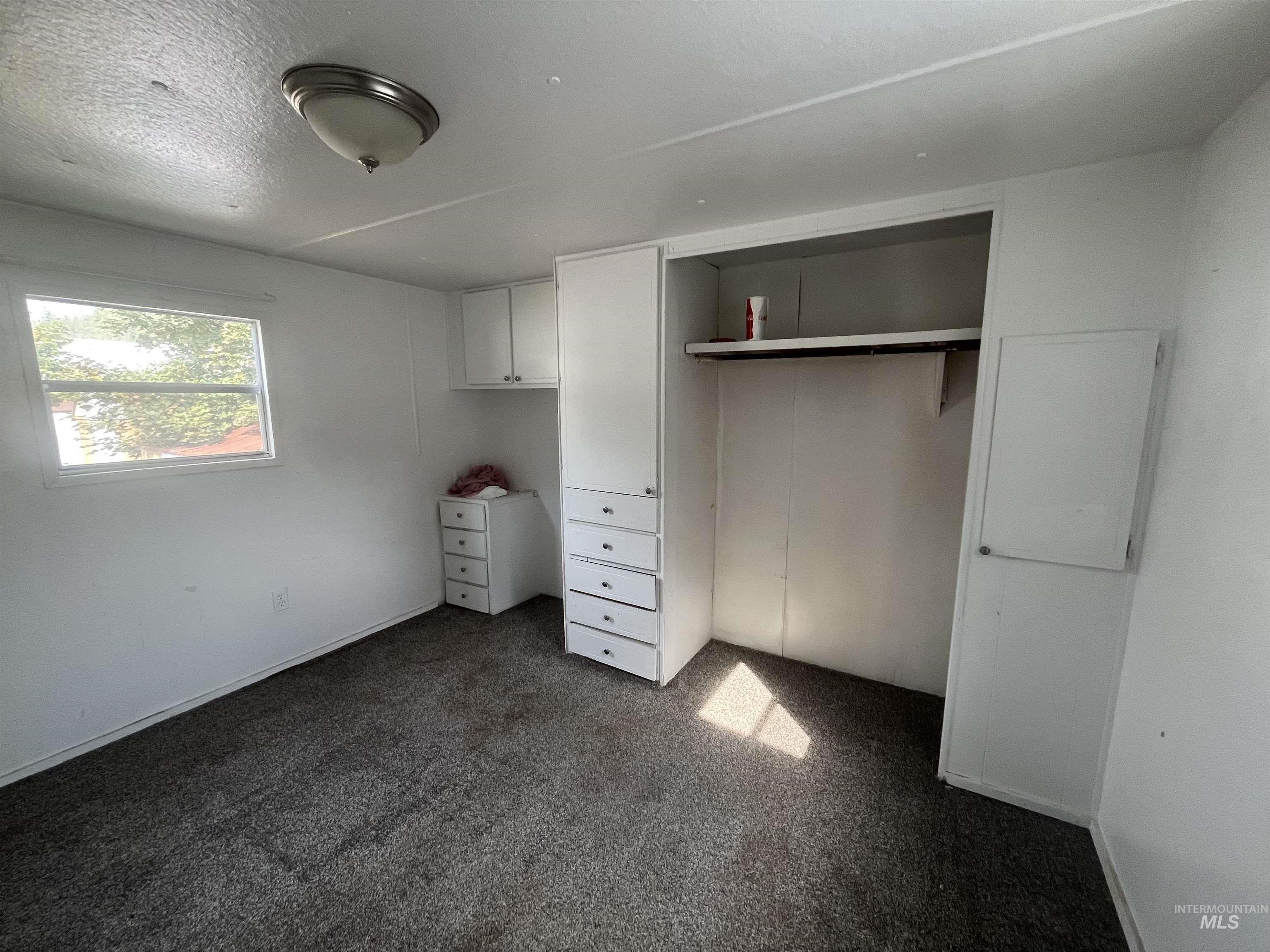 Unfurnished bedroom with dark carpet, a closet, and a textured ceiling