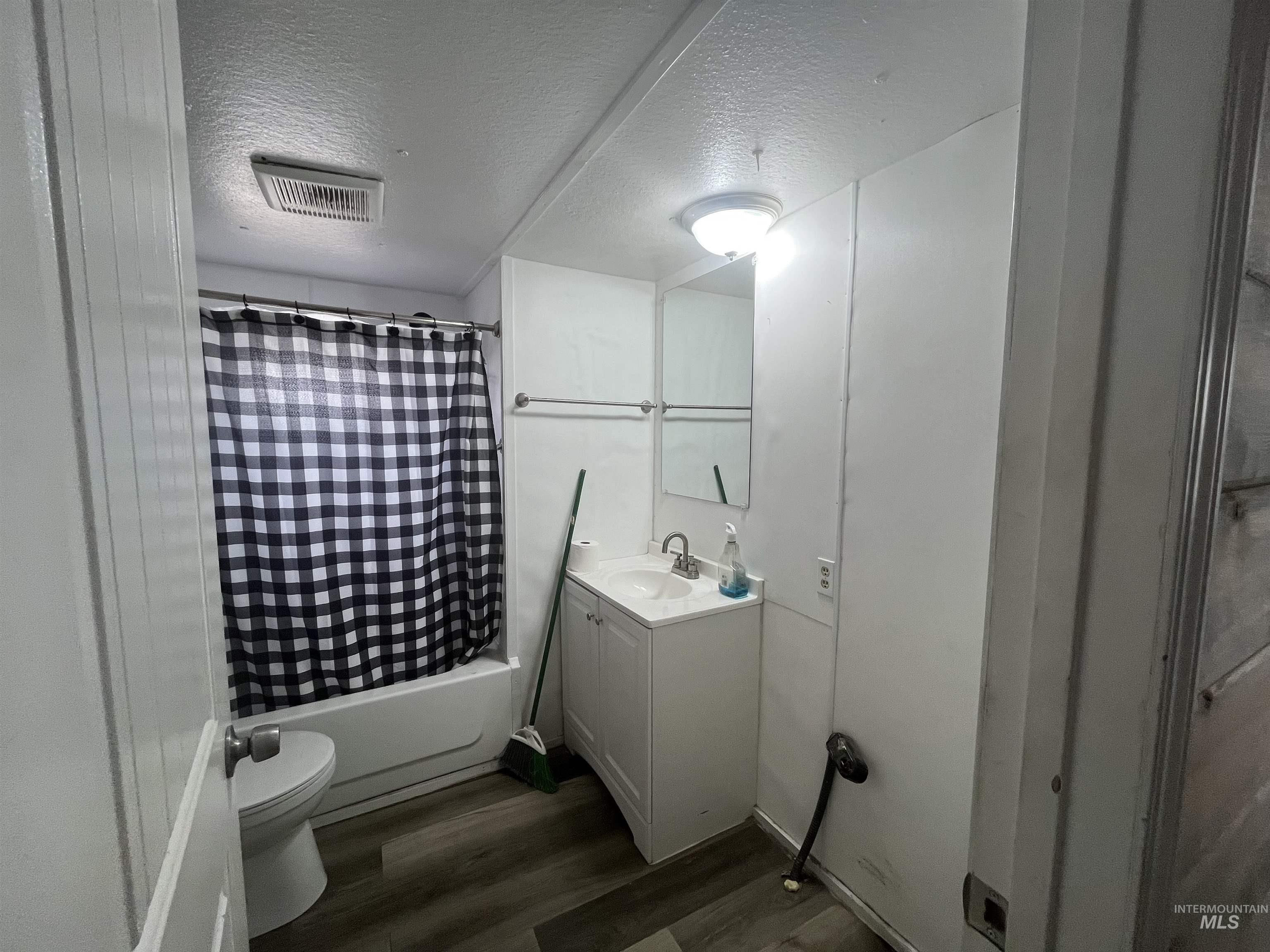 Full bath with a textured ceiling, vanity, shower / tub combo with curtain, and dark wood-type flooring