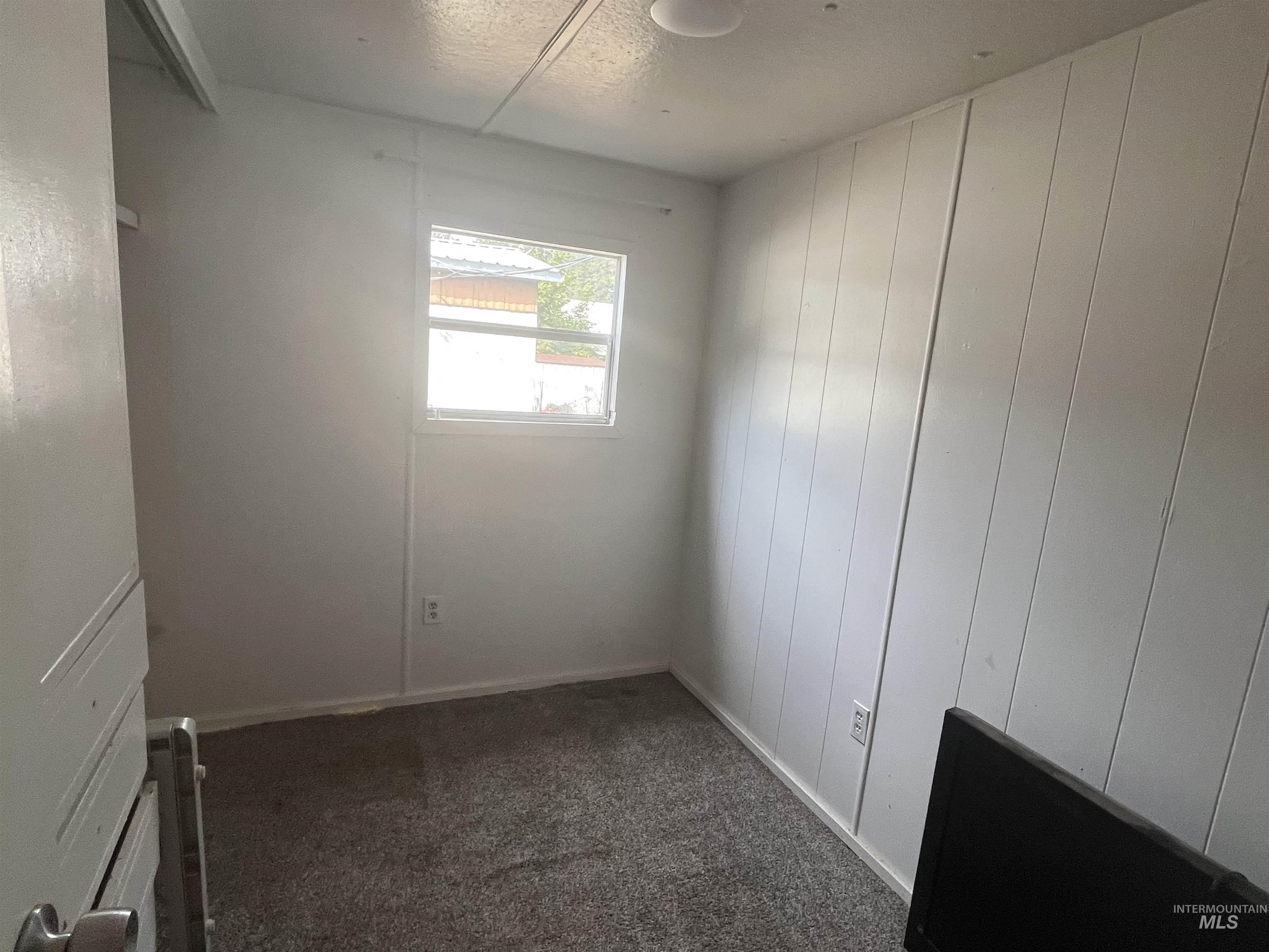 Empty room with dark colored carpet, a textured ceiling, and wooden walls