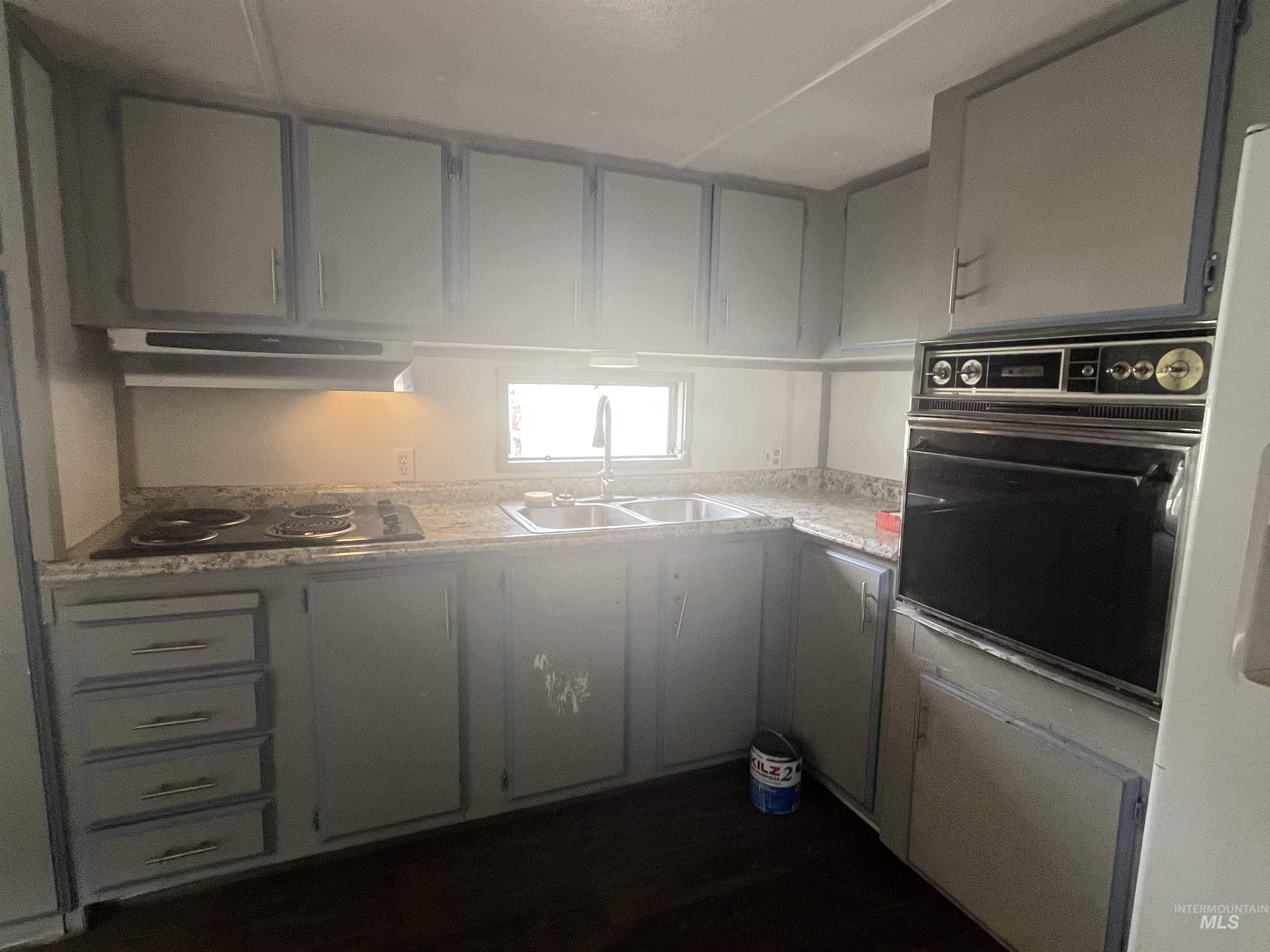 Kitchen with light countertops, black appliances, gray cabinets, and under cabinet range hood