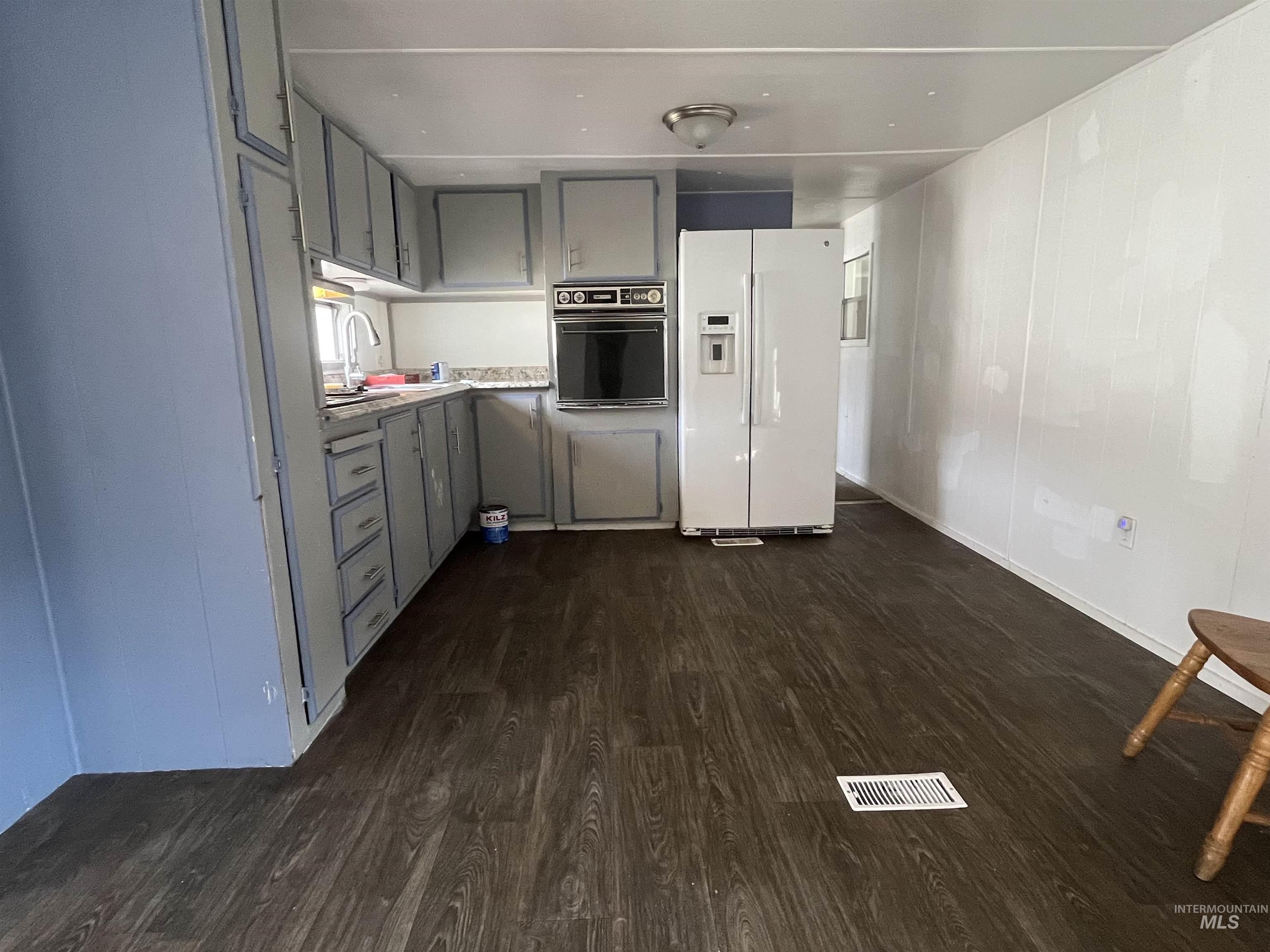 Kitchen with gray cabinets, white refrigerator with ice dispenser, oven, light countertops, and dark wood-style flooring