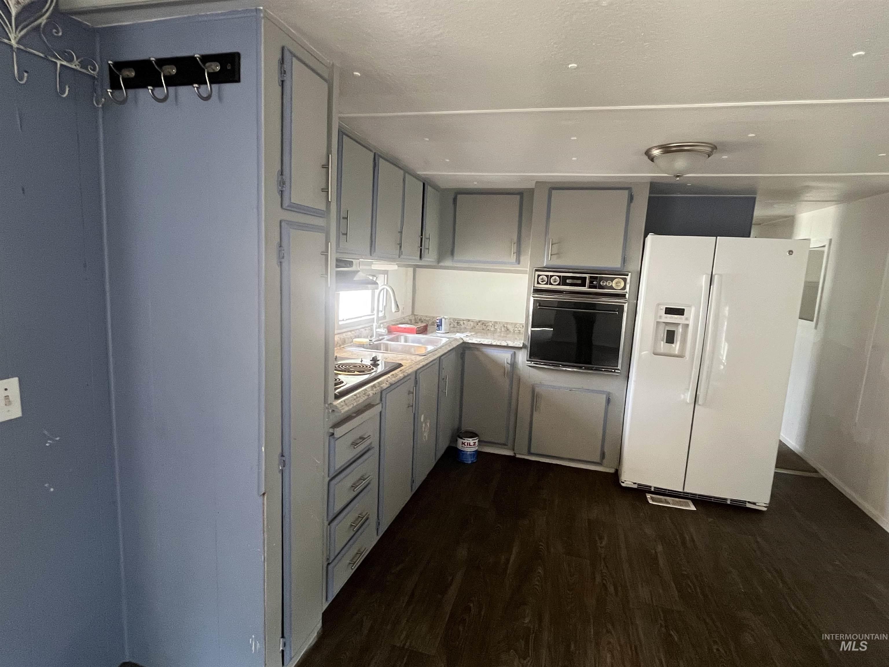 Kitchen featuring white fridge with ice dispenser, dark wood-style floors, light countertops, black oven, and gray cabinetry
