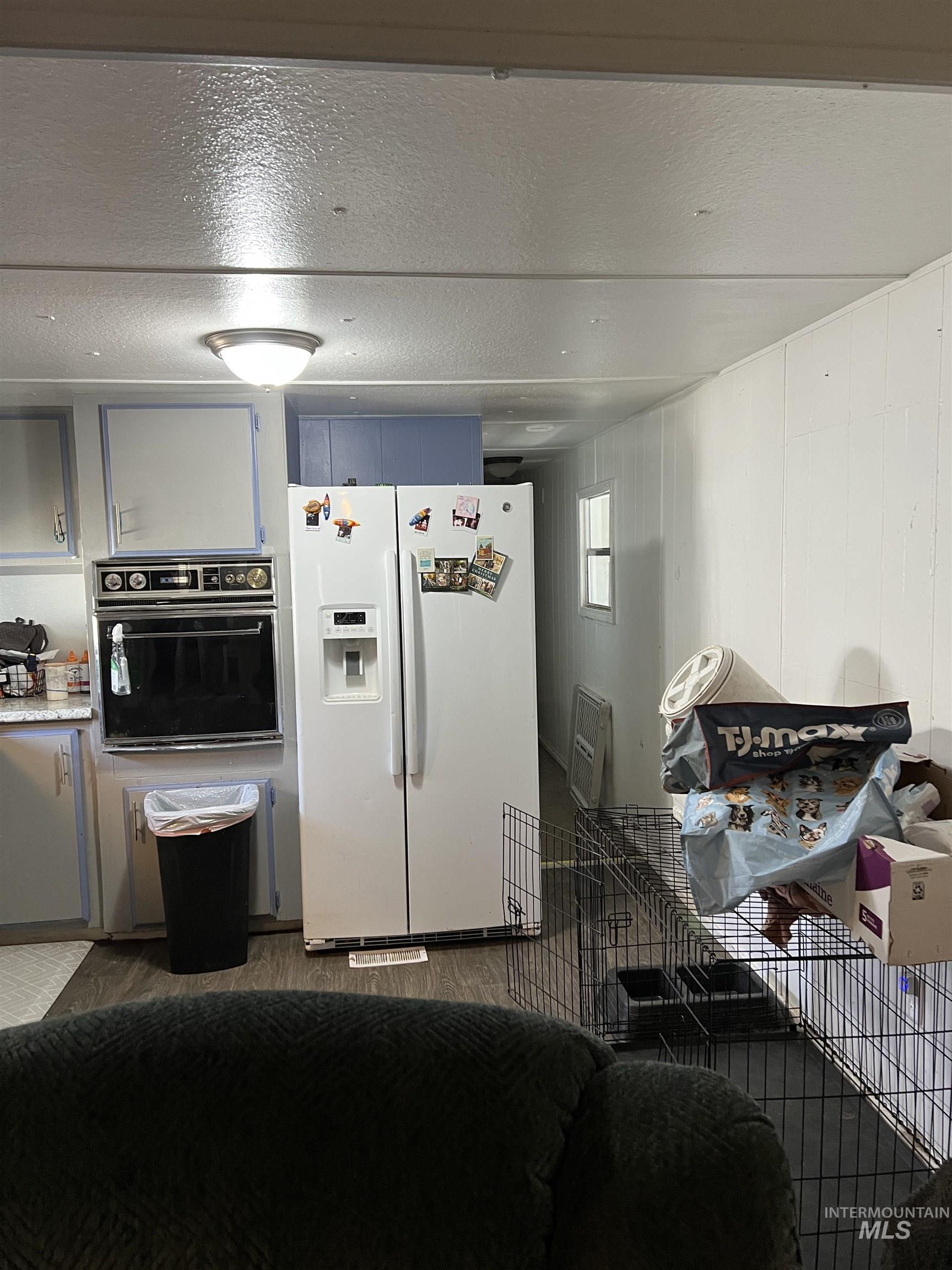 Kitchen featuring white fridge with ice dispenser, black oven, a textured ceiling, blue cabinetry, and light countertops