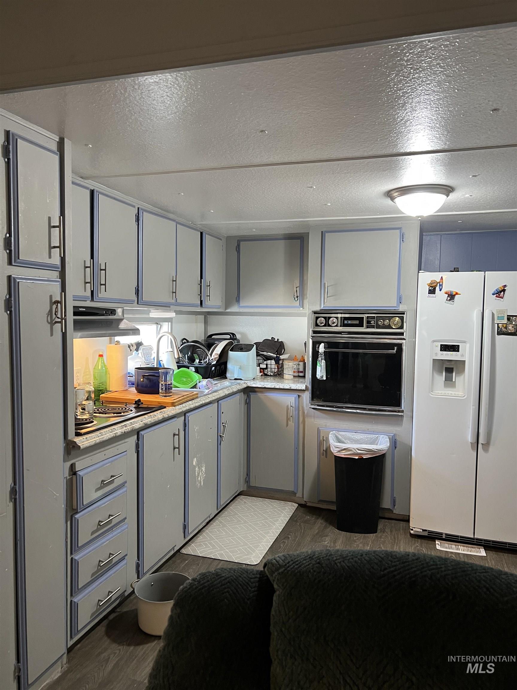 Kitchen featuring a textured ceiling, white refrigerator with ice dispenser, light countertops, oven, and dark wood-style floors
