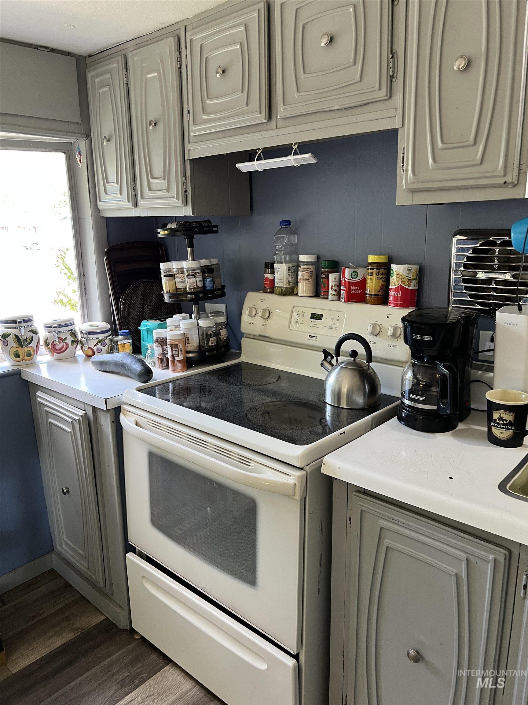 Kitchen featuring white range with electric stovetop, light countertops, gray cabinets, and dark wood-style floors