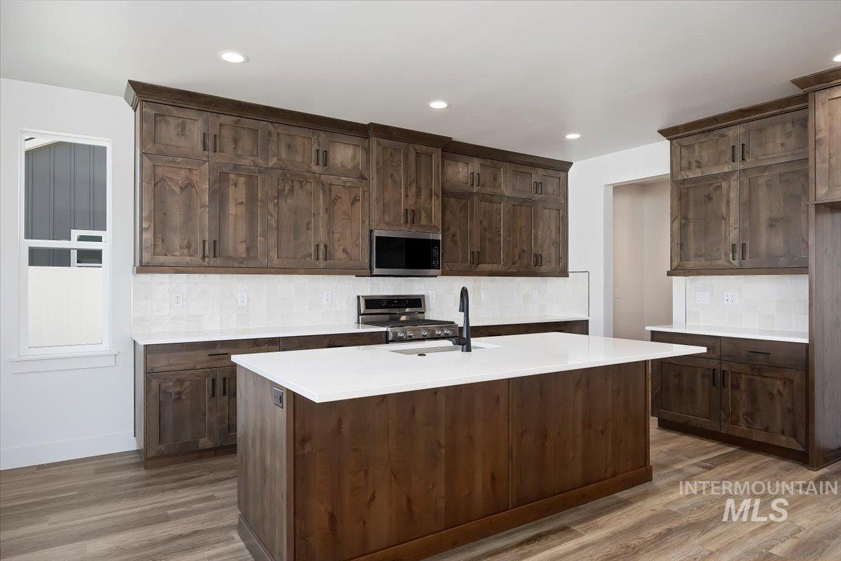 Kitchen with backsplash, stainless steel appliances, wood finished floors, dark brown cabinets, and recessed lighting