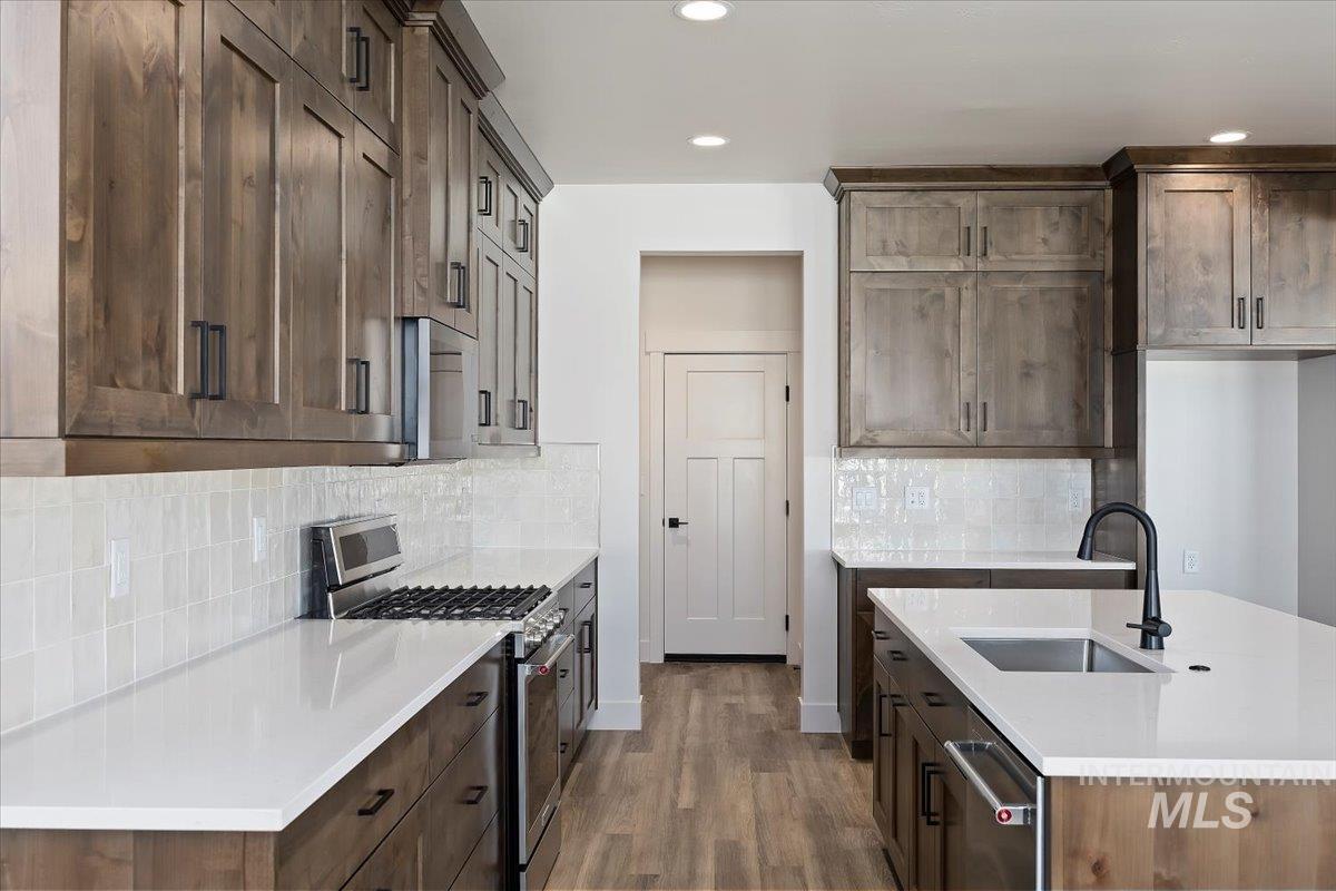 Kitchen with appliances with stainless steel finishes, backsplash, dark wood finished floors, light stone countertops, and a center island with sink