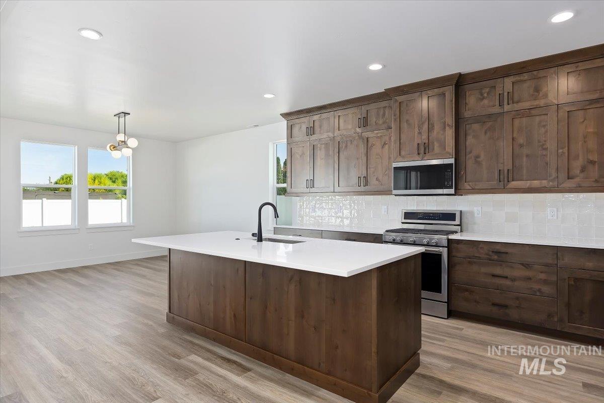 Kitchen featuring appliances with stainless steel finishes, pendant lighting, decorative backsplash, recessed lighting, and an island with sink