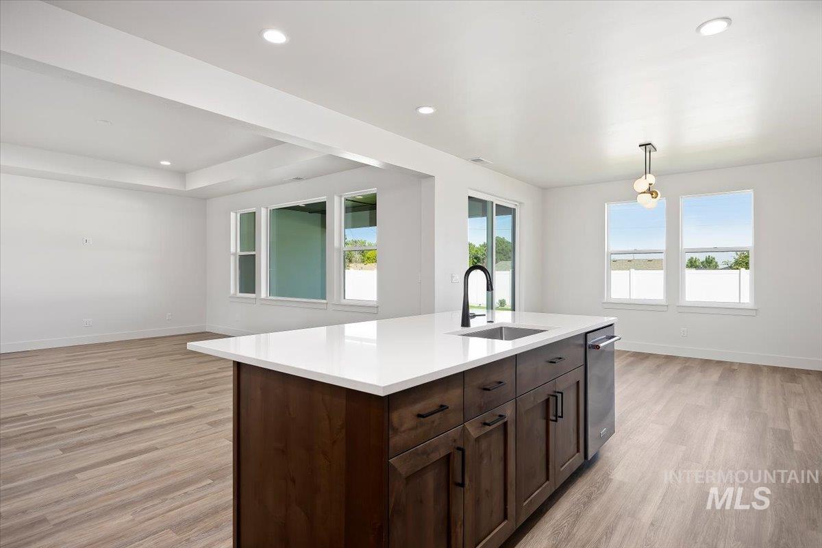 Kitchen featuring pendant lighting, dark brown cabinets, open floor plan, light wood-style flooring, and recessed lighting