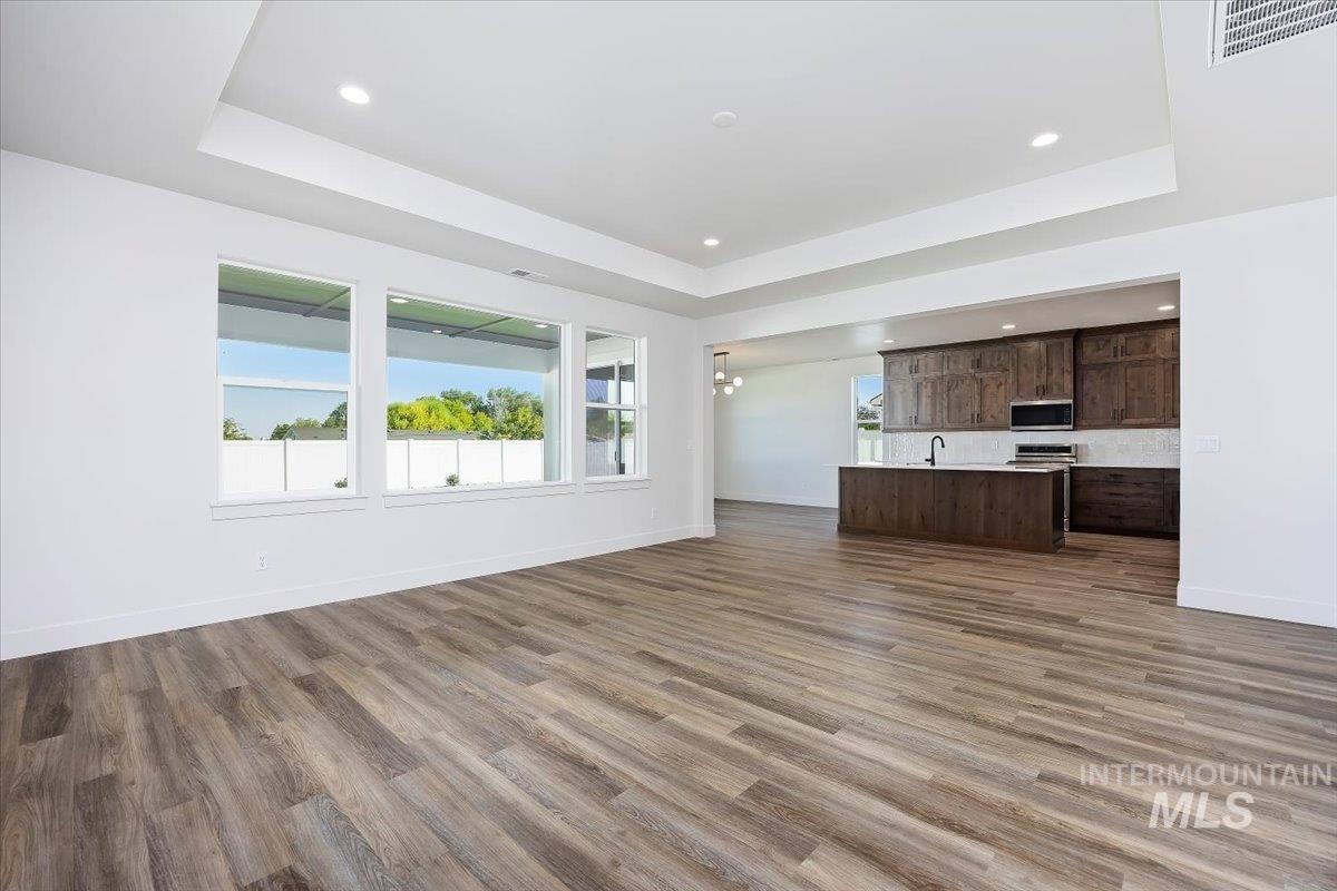 Unfurnished living room with a raised ceiling, dark wood-style floors, recessed lighting, and a chandelier