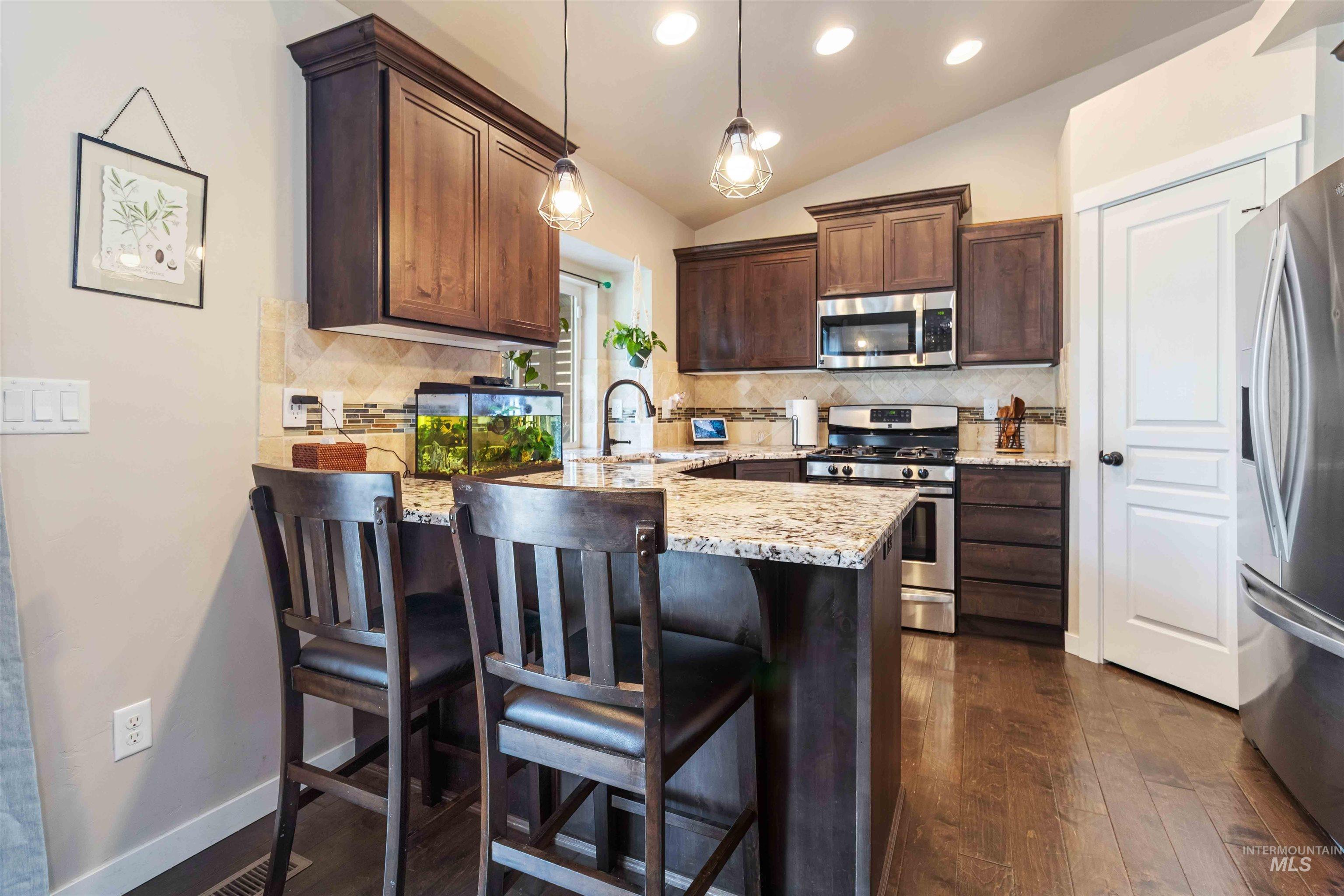 Kitchen featuring dark brown cabinetry, stainless steel appliances, decorative backsplash, light stone countertops, and pendant lighting