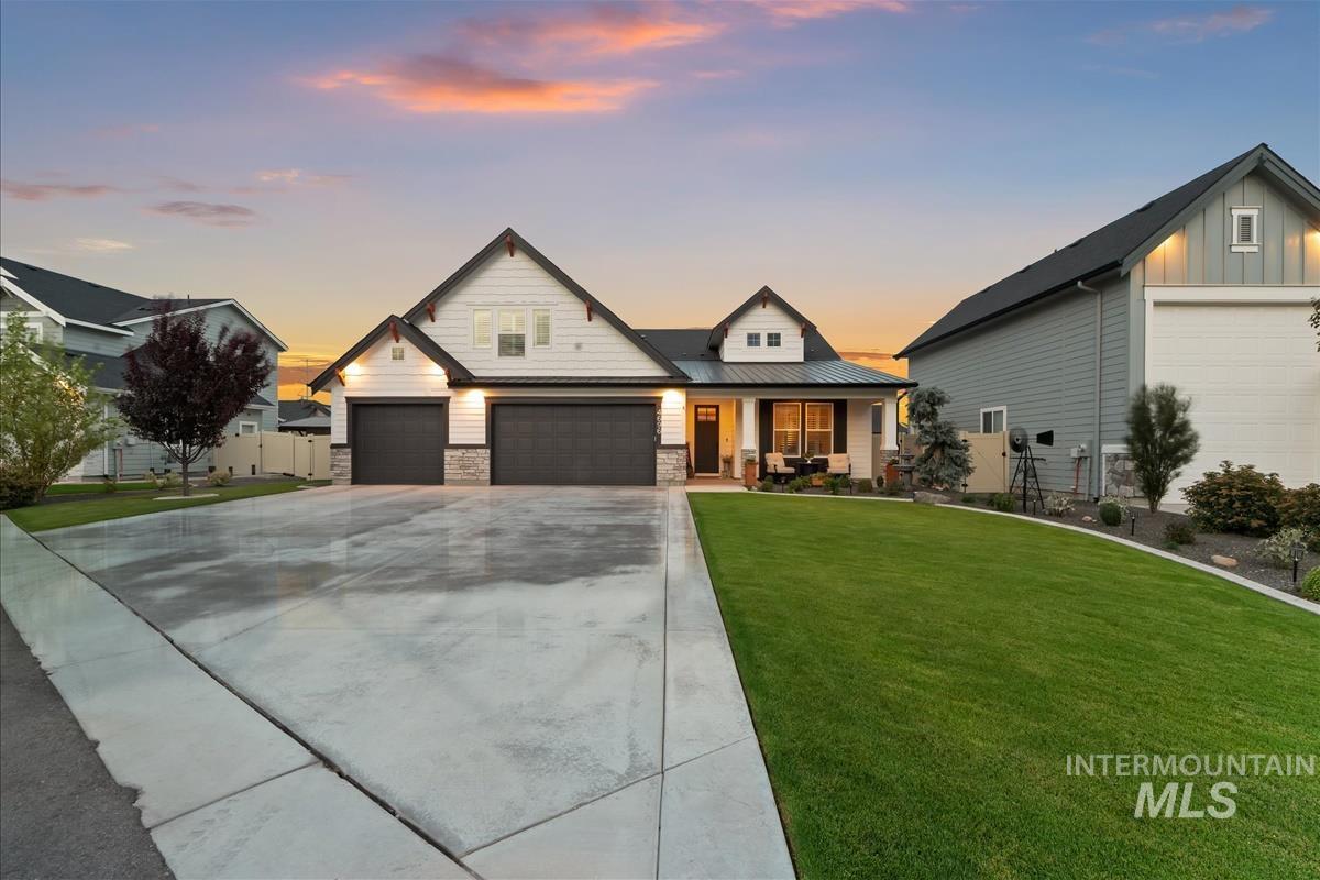 View of front of home with covered porch, stone siding, driveway, a metal roof, and an attached garage
