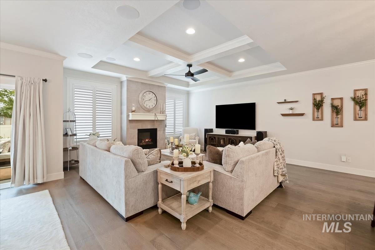 Living room featuring a fireplace, wood finished floors, coffered ceiling, crown molding, and beamed ceiling