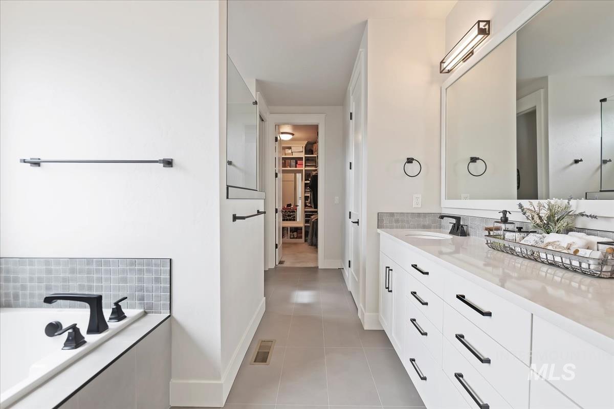 Full bathroom featuring a spacious closet, vanity, light tile patterned floors, a garden tub, and tasteful backsplash