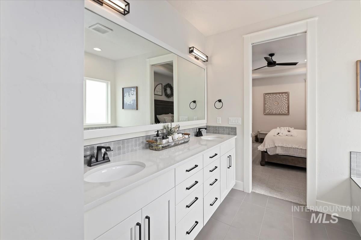 Ensuite bathroom featuring double vanity, light tile patterned flooring, and a ceiling fan