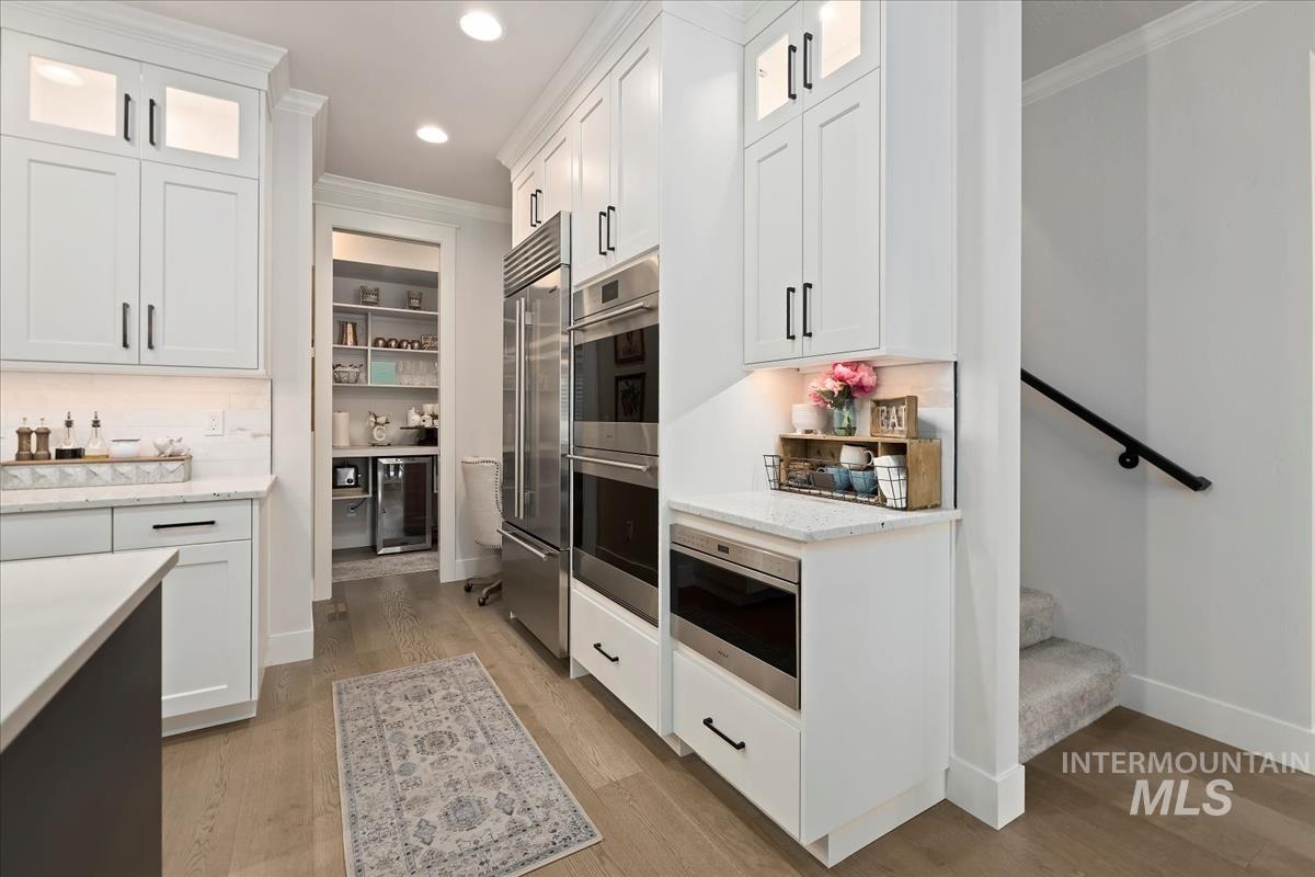 Kitchen with glass insert cabinets, light wood-style flooring, ornamental molding, white cabinetry, and built in appliances